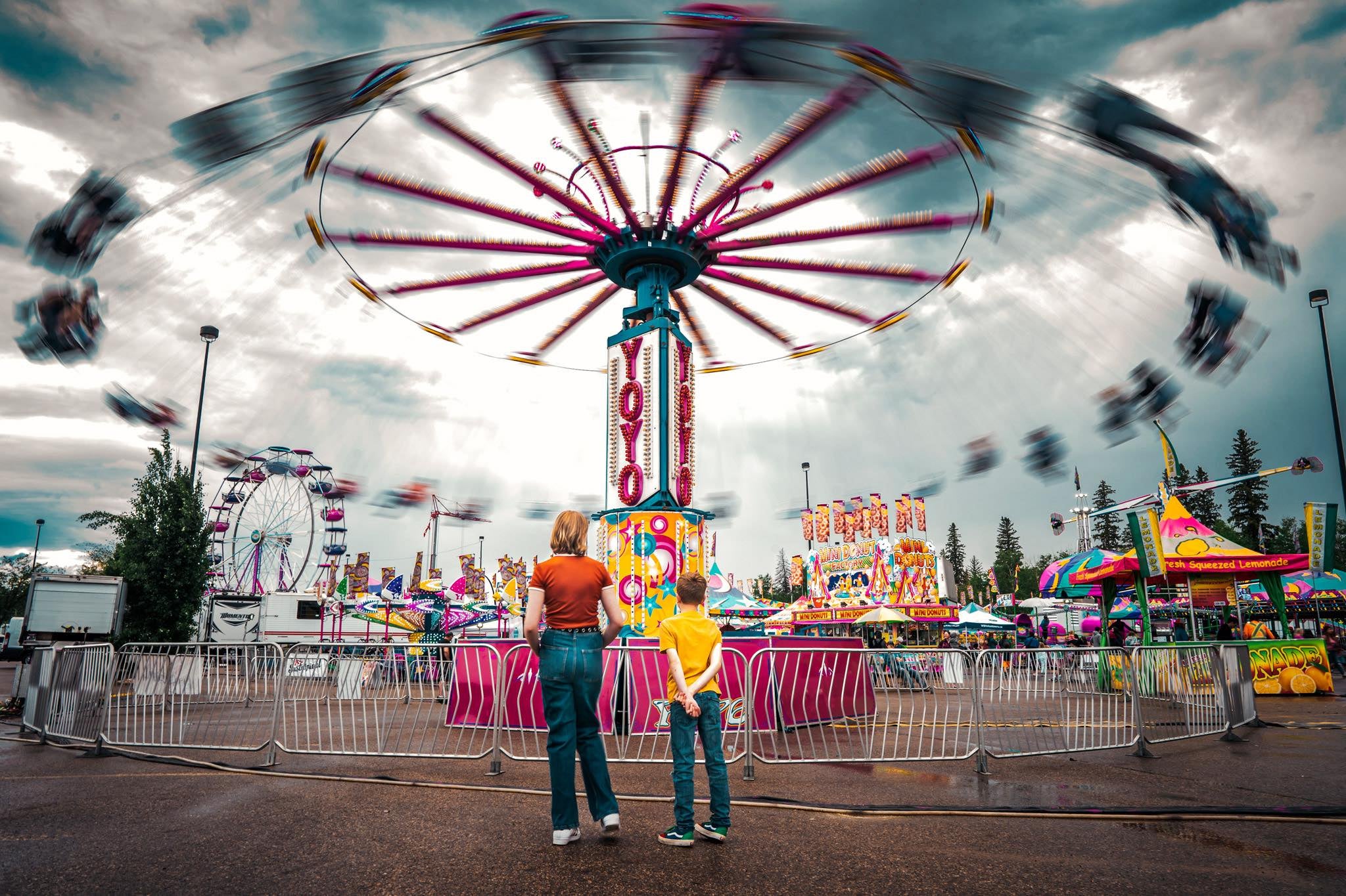 Woman and boy stand watching a carnival ride