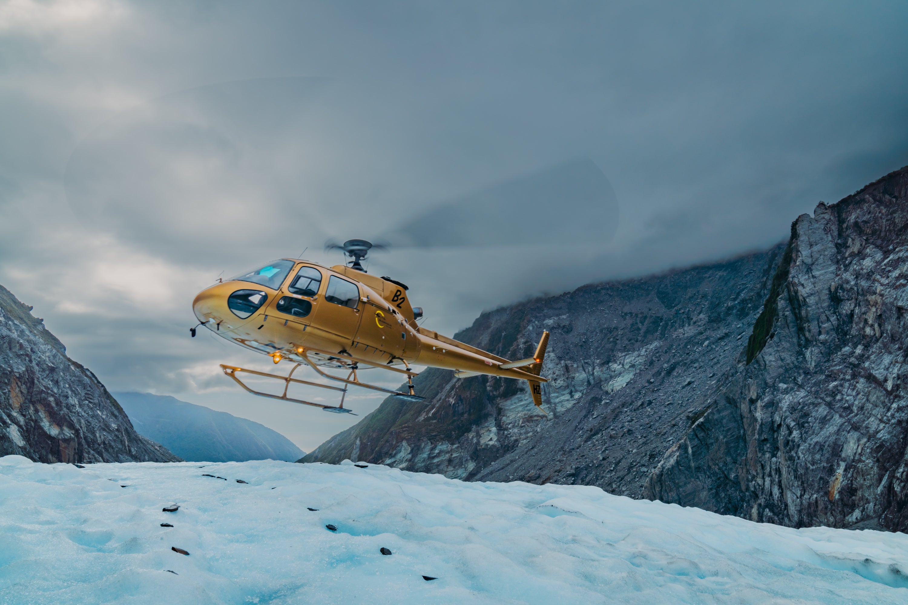 Yellow helicopter flying off of snowy mountain