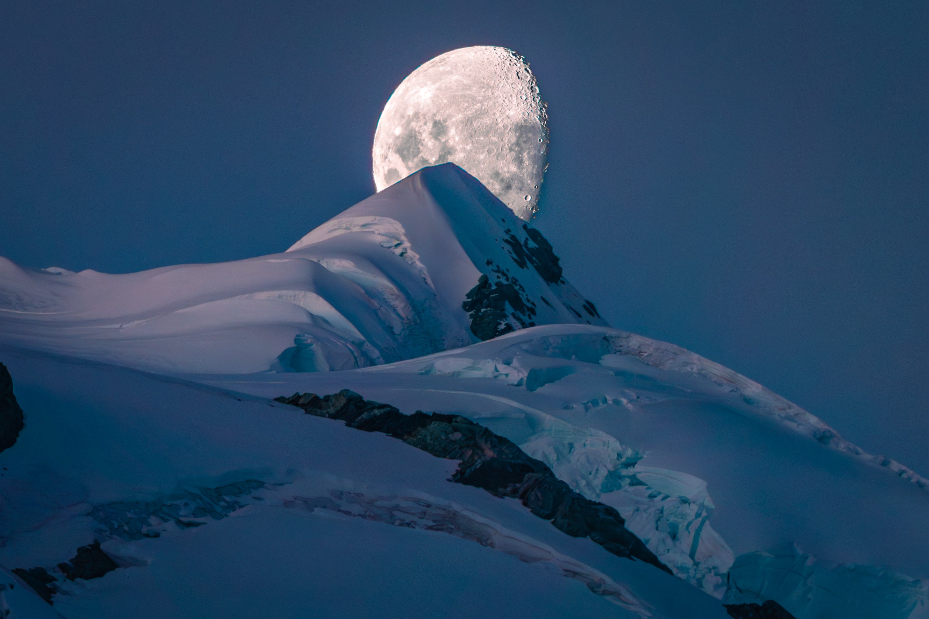Large moon in the background of snowy mountain peak