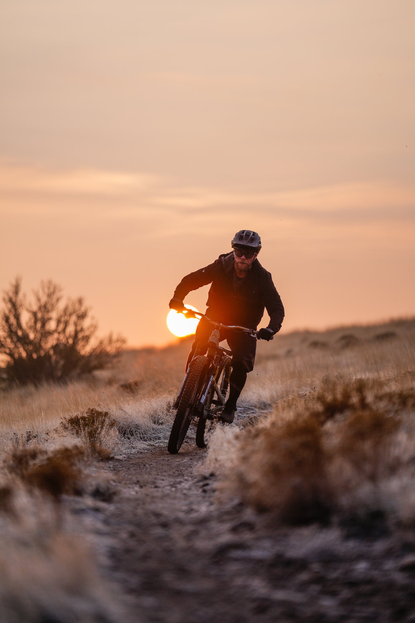 Mountain biker riding on a desert trail at sunset.