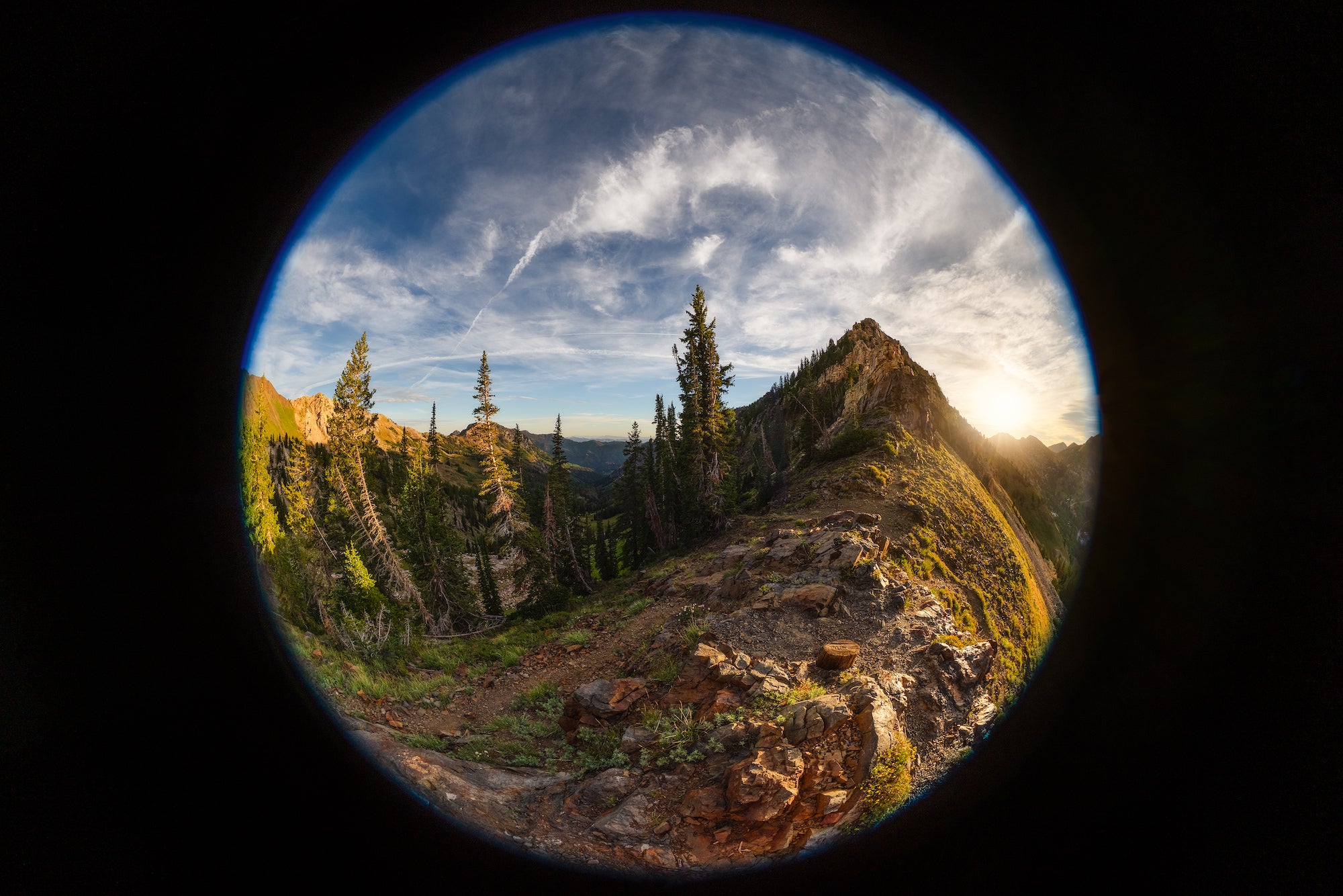 Circular fisheye view of a rocky mountain ridge and evergreen valley at sunset, photographed by Autumn Schrock.