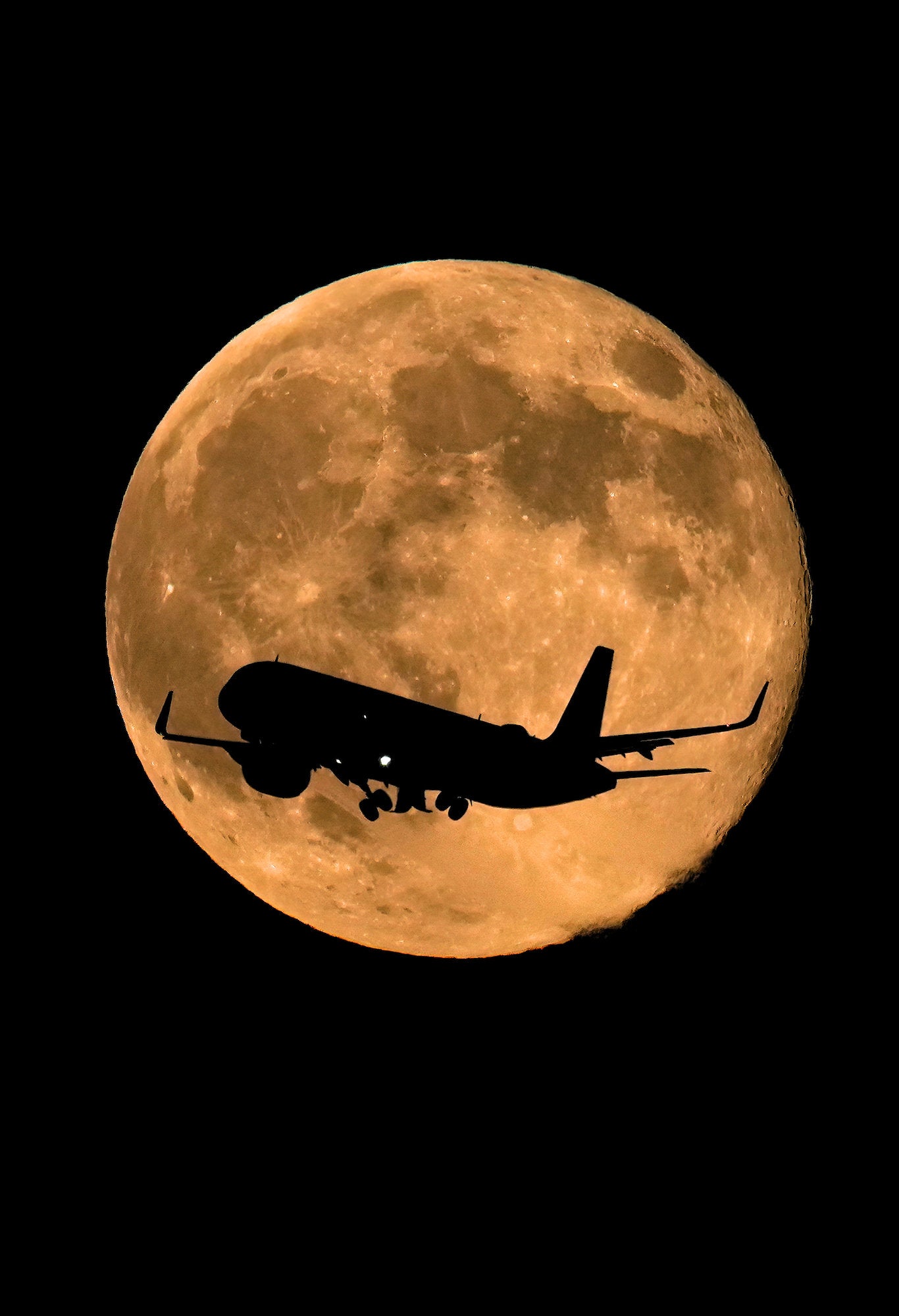 Silhouette of a passenger airplane crossing a golden supermoon above Chicago’s night sky.
