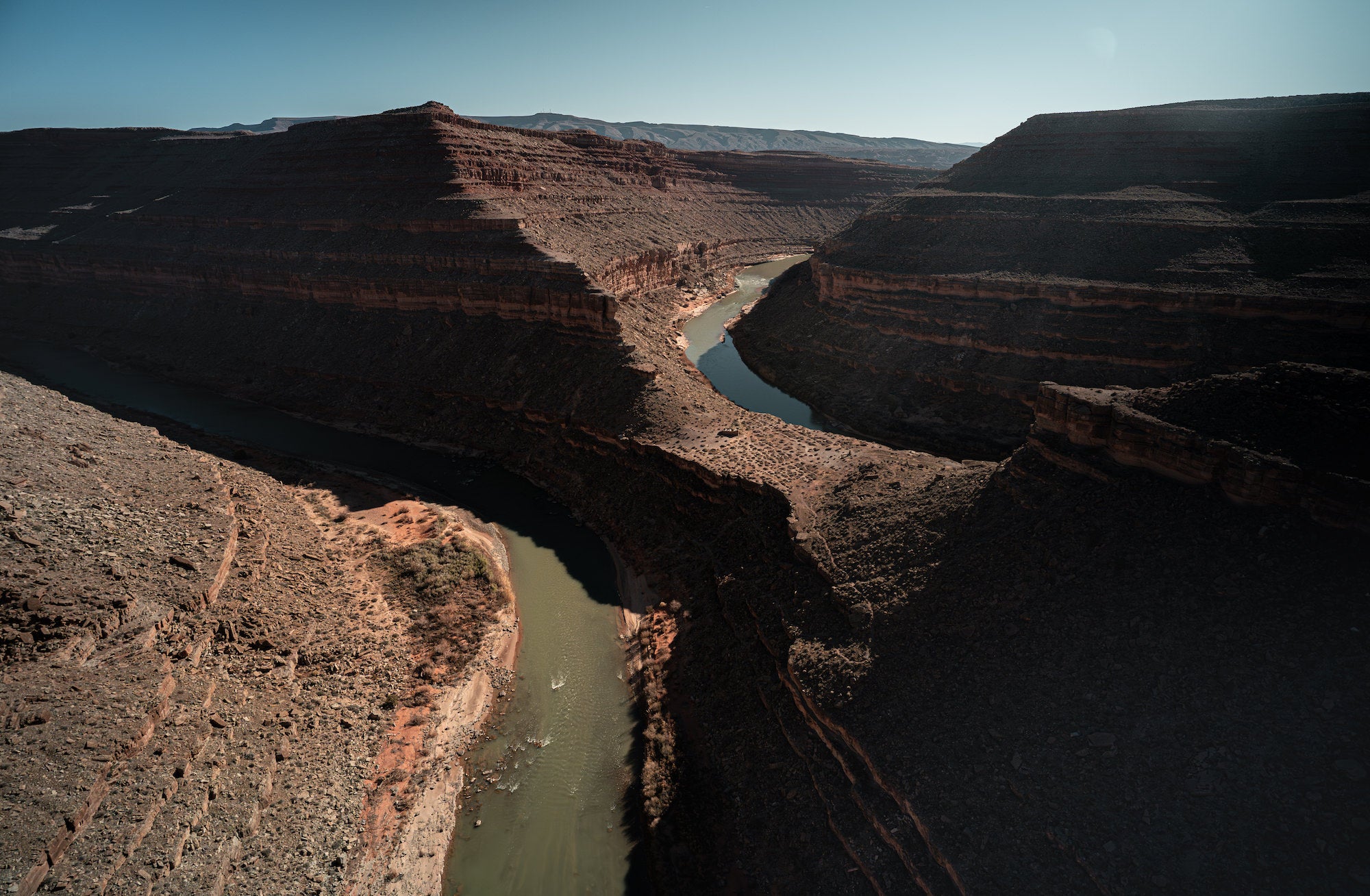 Aerial view of the green San Juan River curving between shadowed desert canyon walls. Photograph by Sydney Smolla.