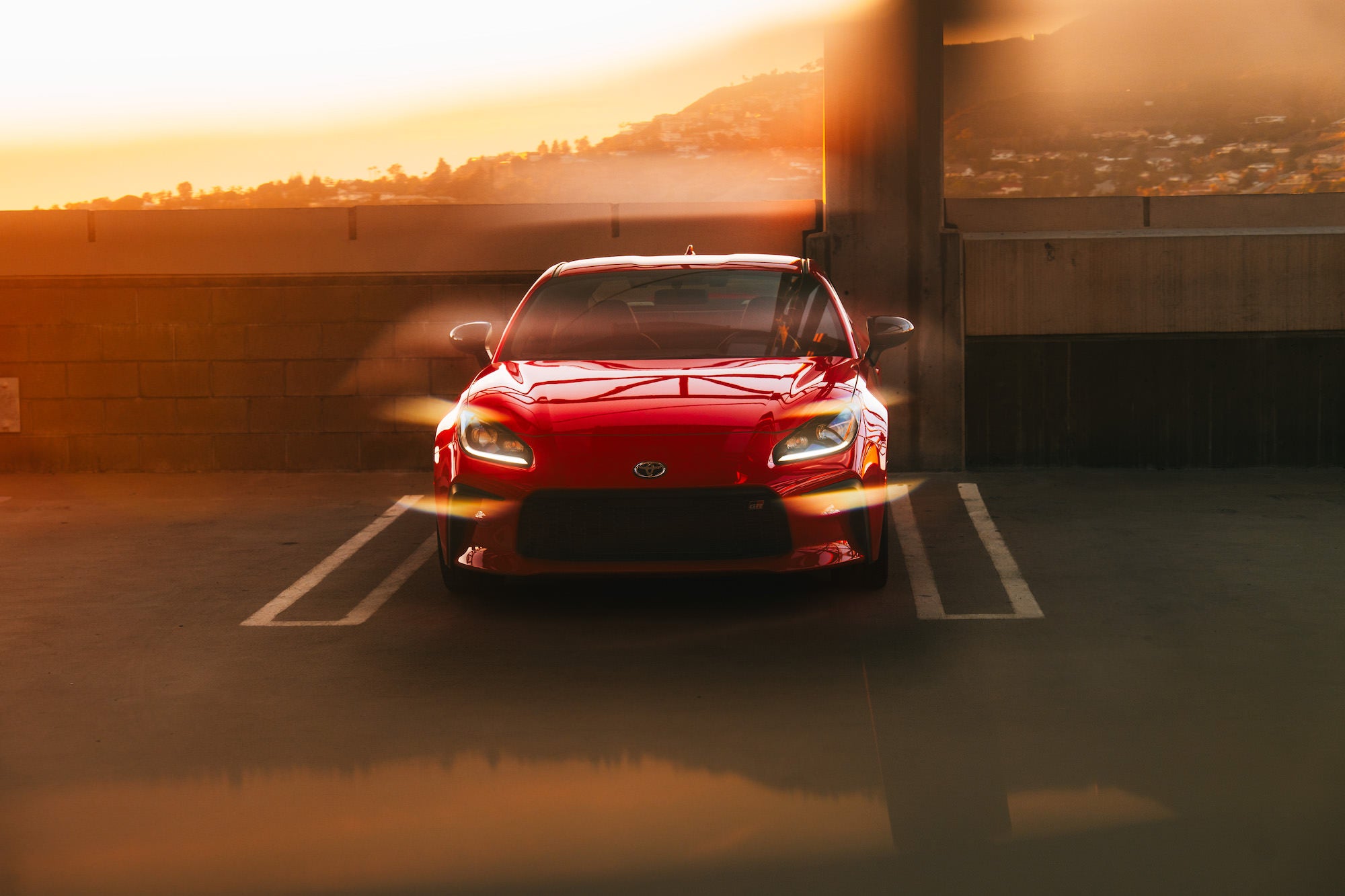 Red sports car in a parking structure at golden hour with sun flares.