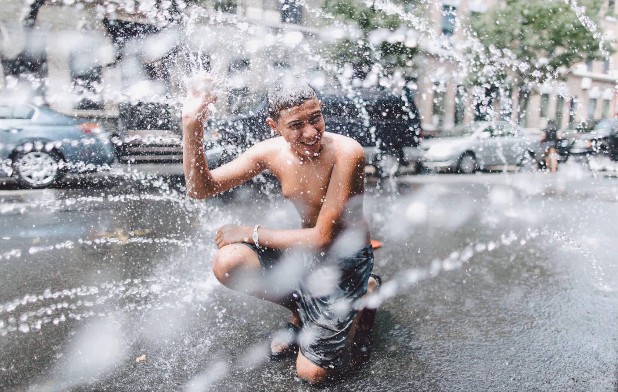 Young man playing outside in the sprinklers with water spraying everywhere.
