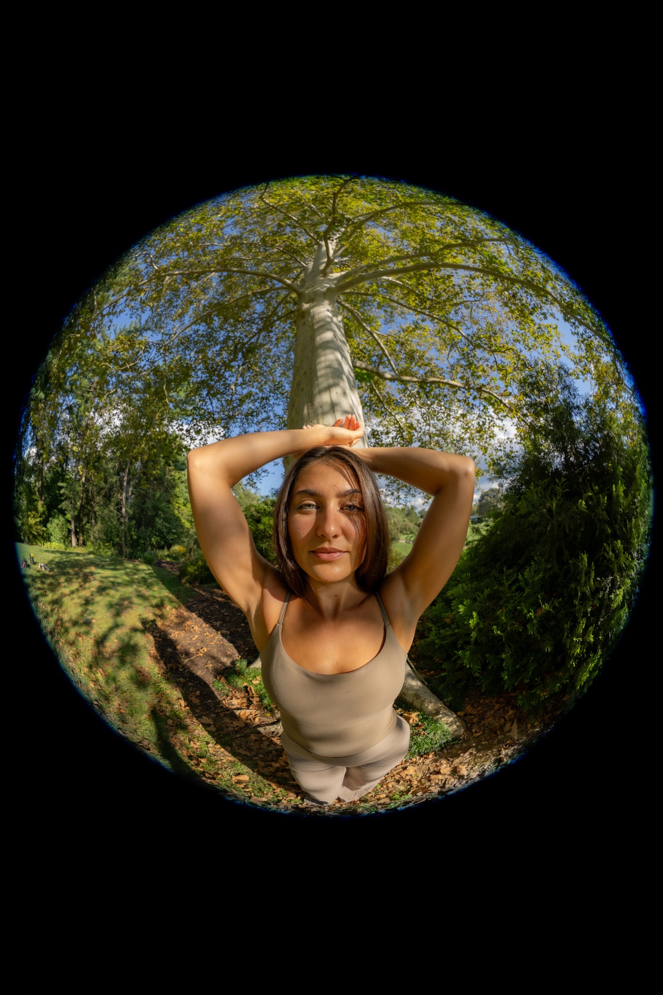 A woman stands beneath a tall tree in a circular fisheye portrait, photographed by Drew Geraci.