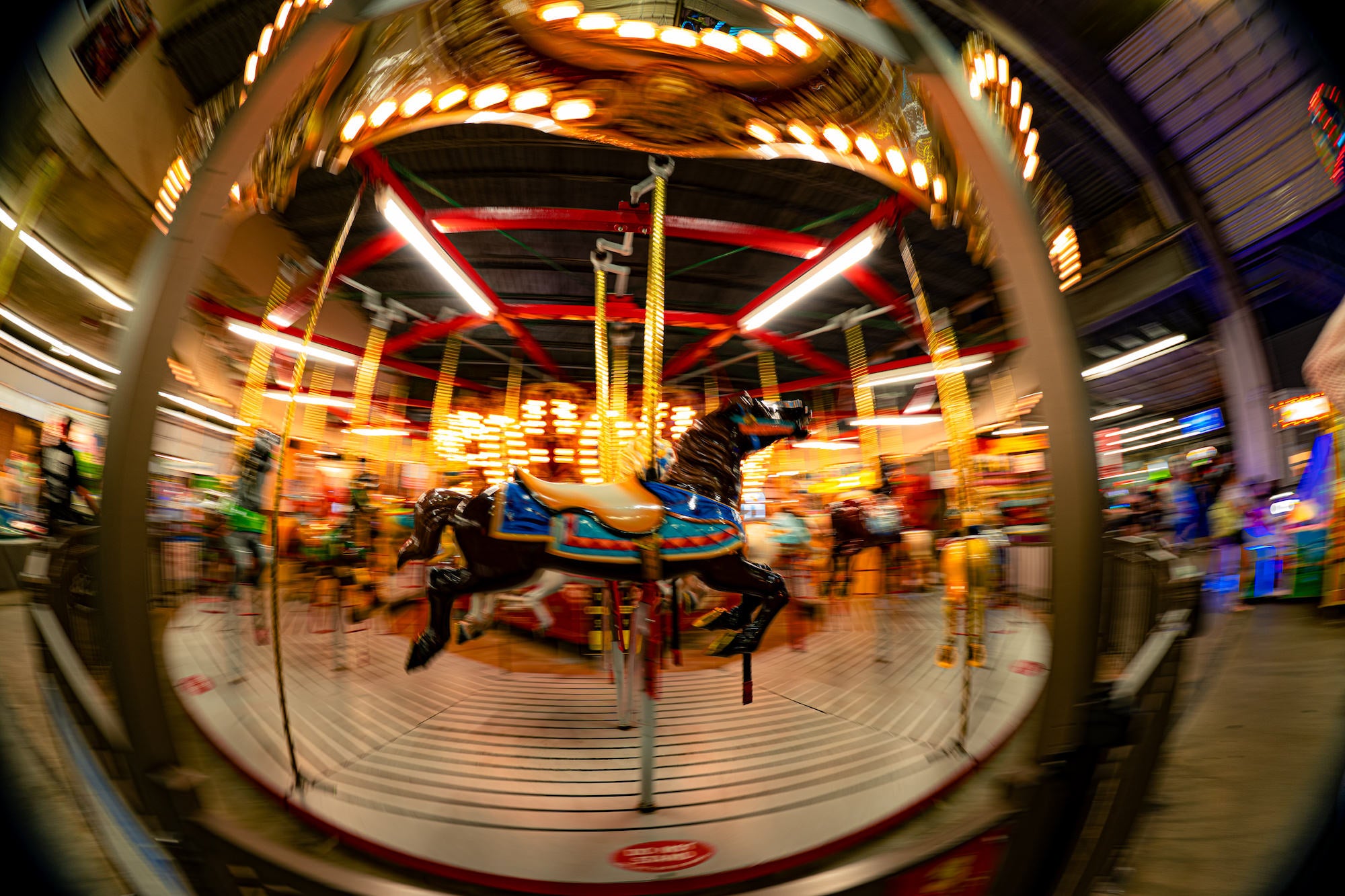A carousel horse spins beneath warm lights in a motion-blurred fisheye view, photographed by Drew Geraci.