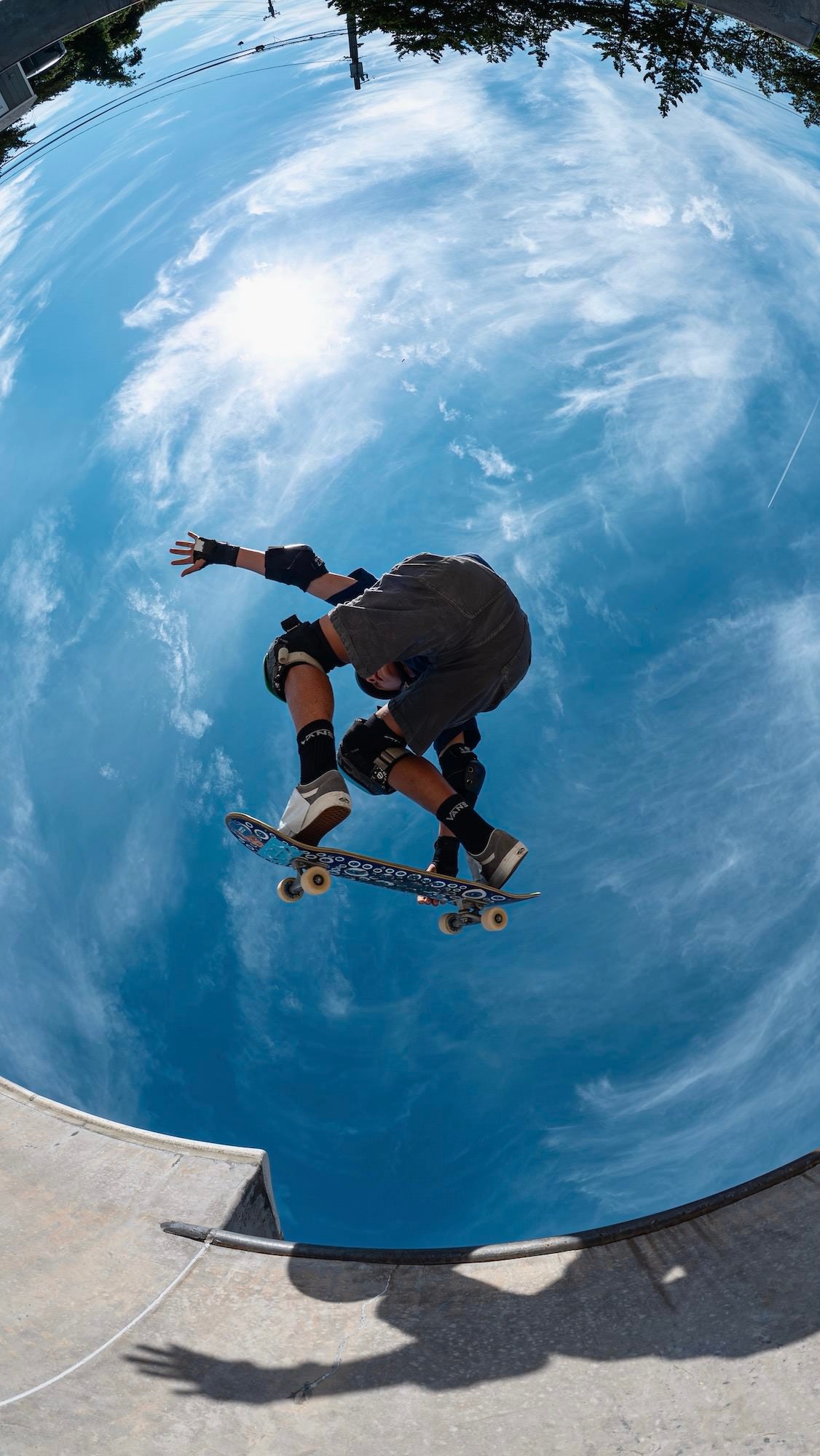 A skateboarder airborne above a concrete bowl against a blue sky, photographed by Allegra Hutton.
