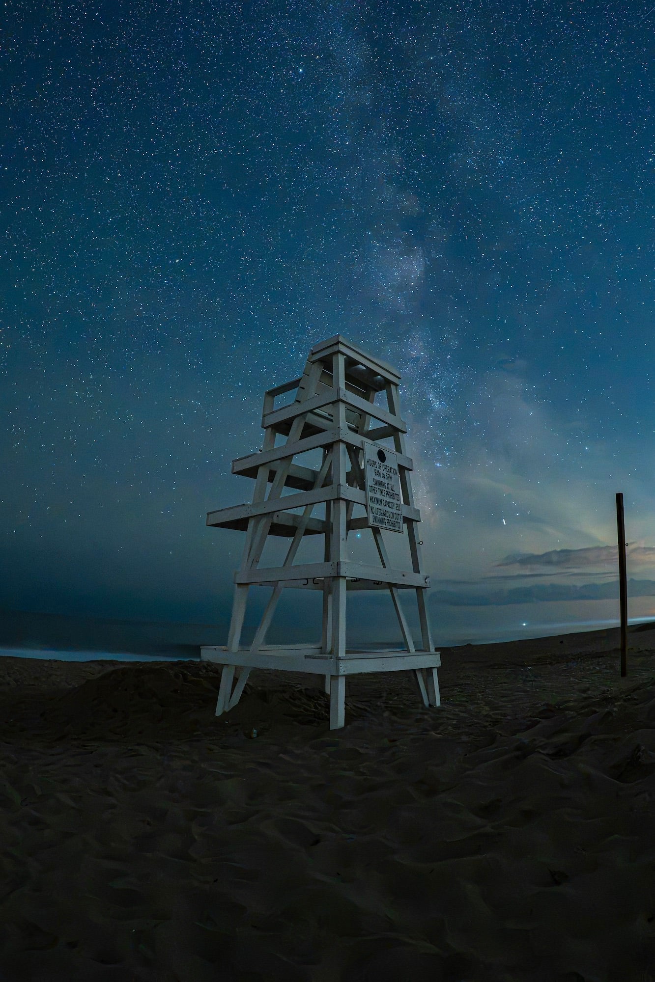 A lifeguard chair stands on a beach beneath a star-filled night sky, photographed by Allegra Hutton.