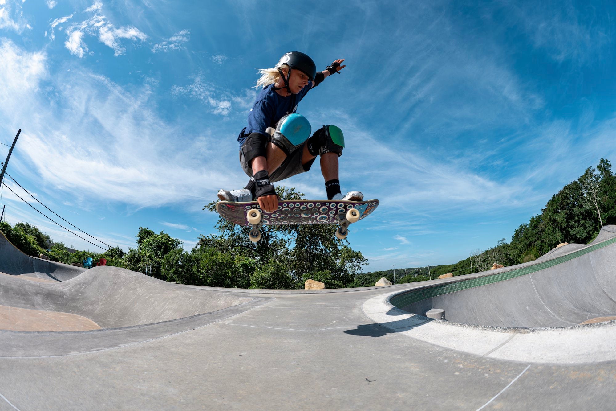 A skateboarder performs an aerial trick above a concrete skatepark, photographed by Allegra Hutton.