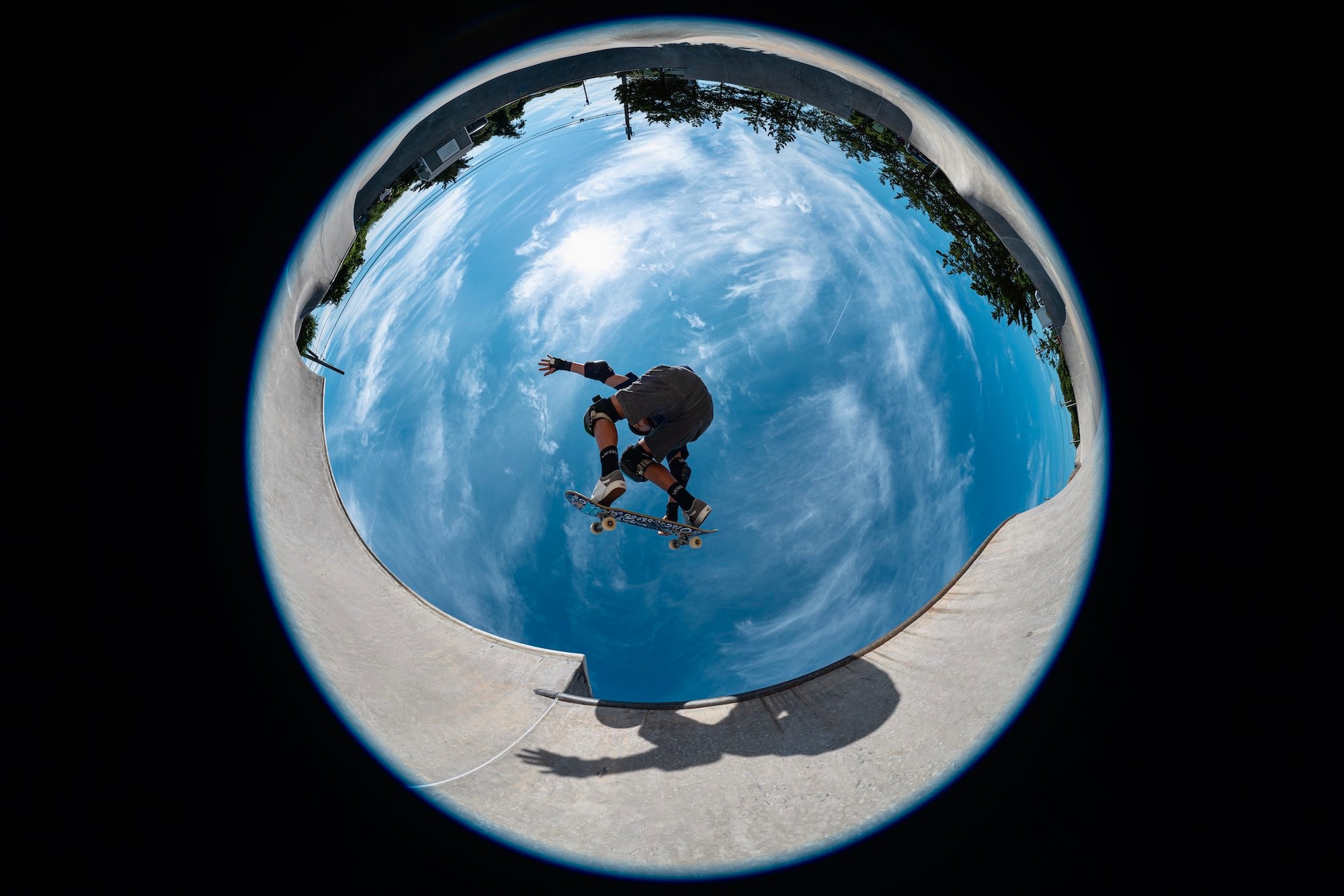 Circular fisheye view of a skateboarder airborne over a concrete bowl, photographed by Allegra Hutton.