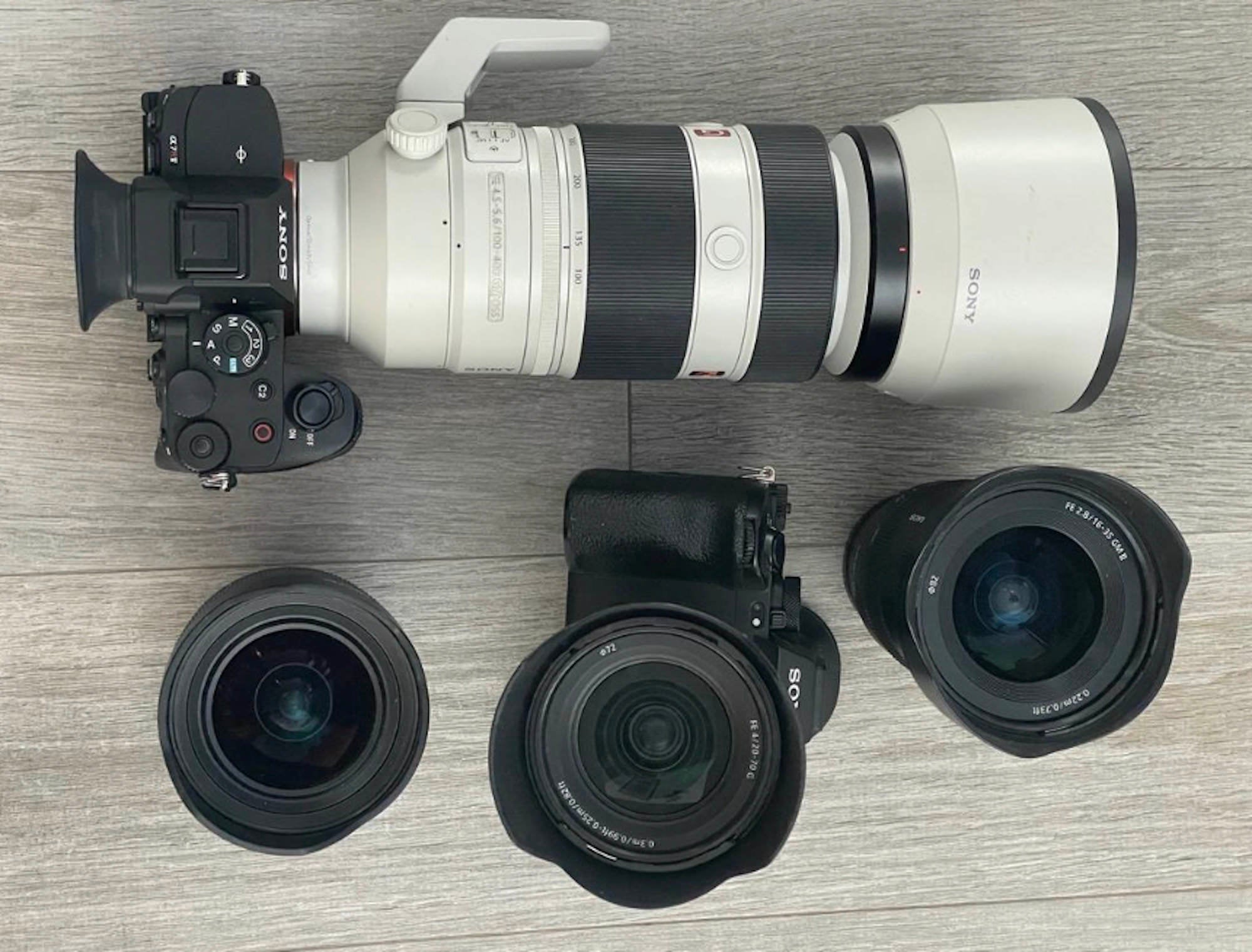 Flat lay of Sony Alpha cameras with telephoto and wide-angle lenses on a light wood floor.