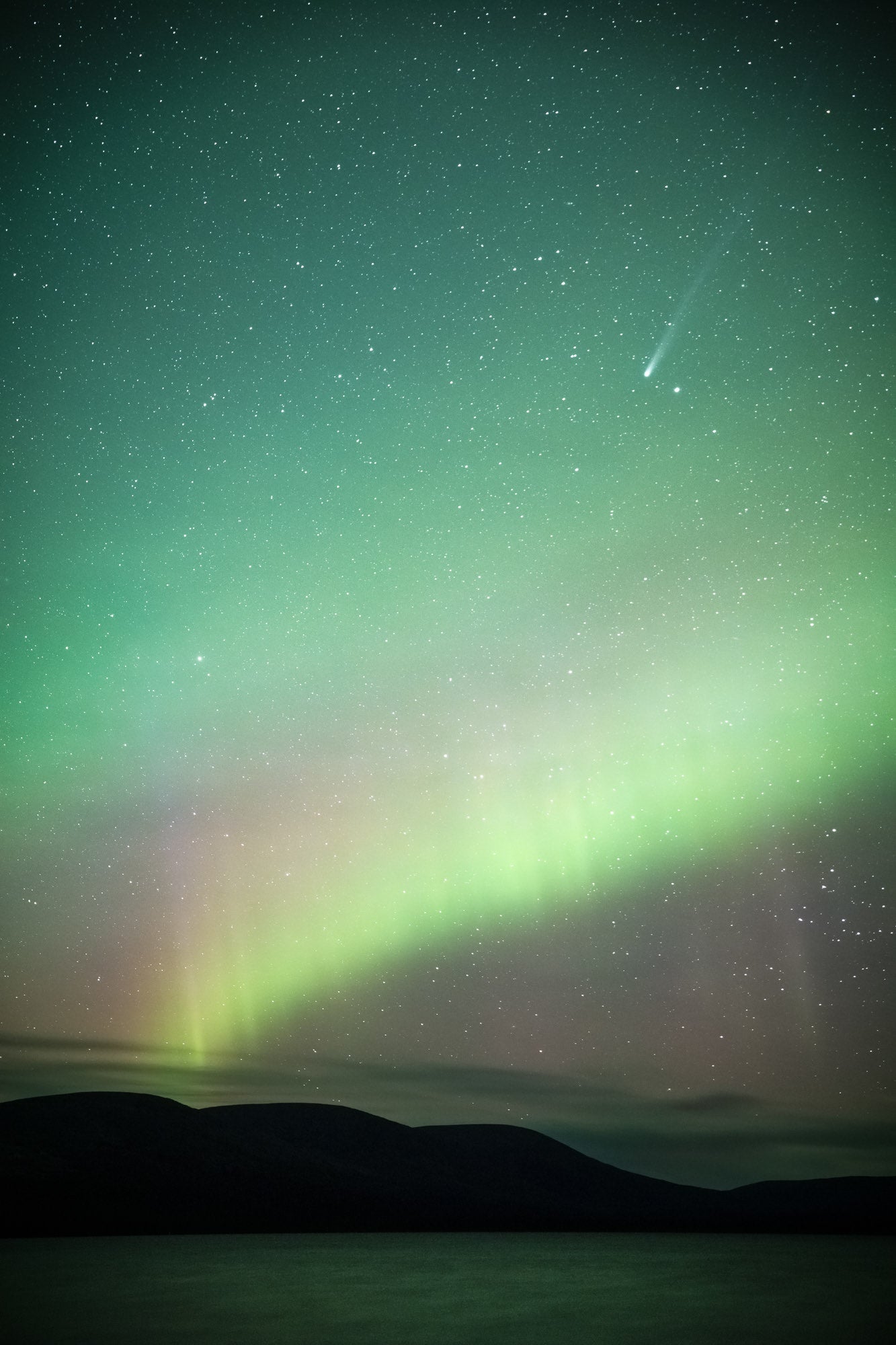 Astro landscape photograph of a comet passing through an aurora-filled sky by Timo Oksanen