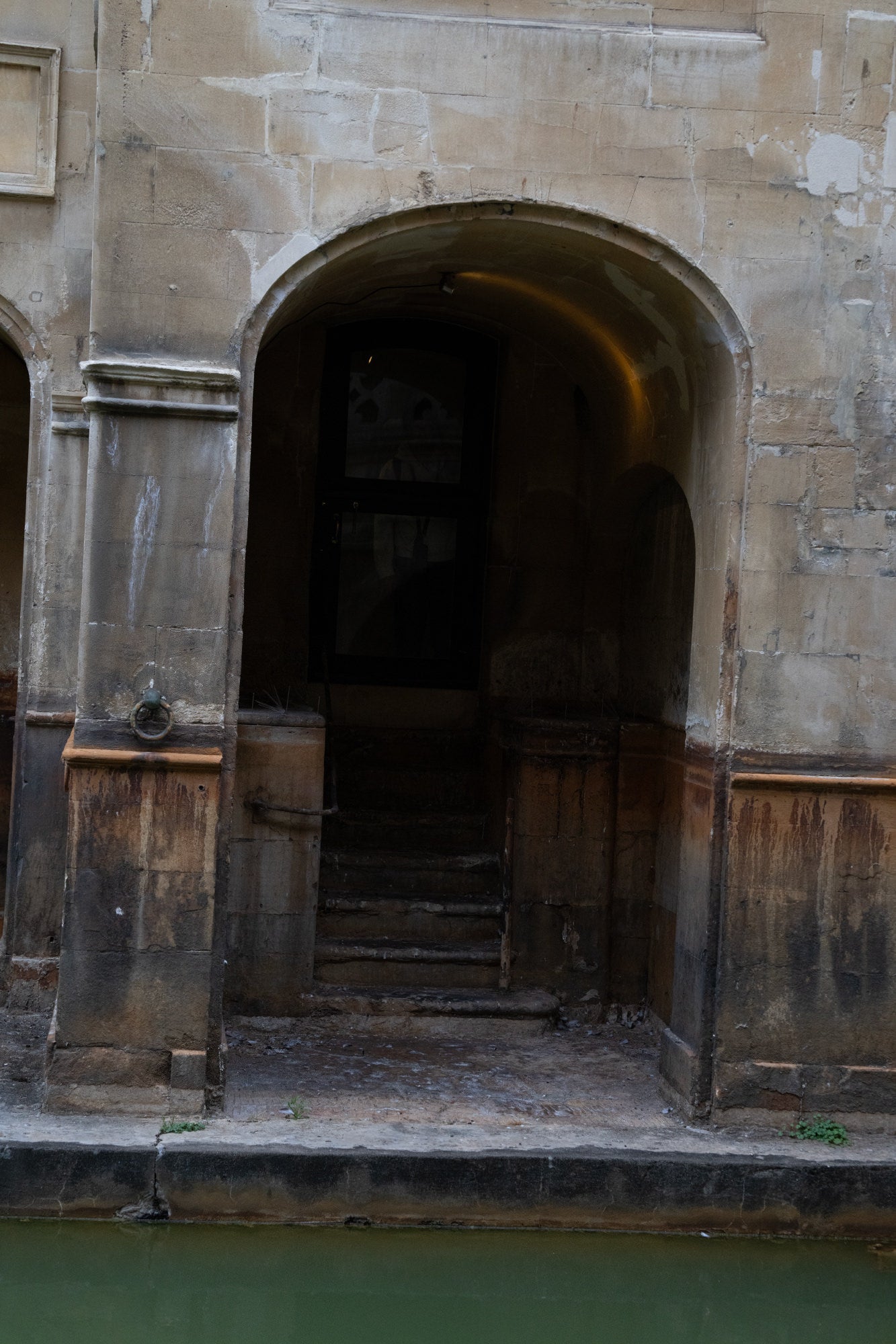 Weathered stone archway with dark steps descending to green water.