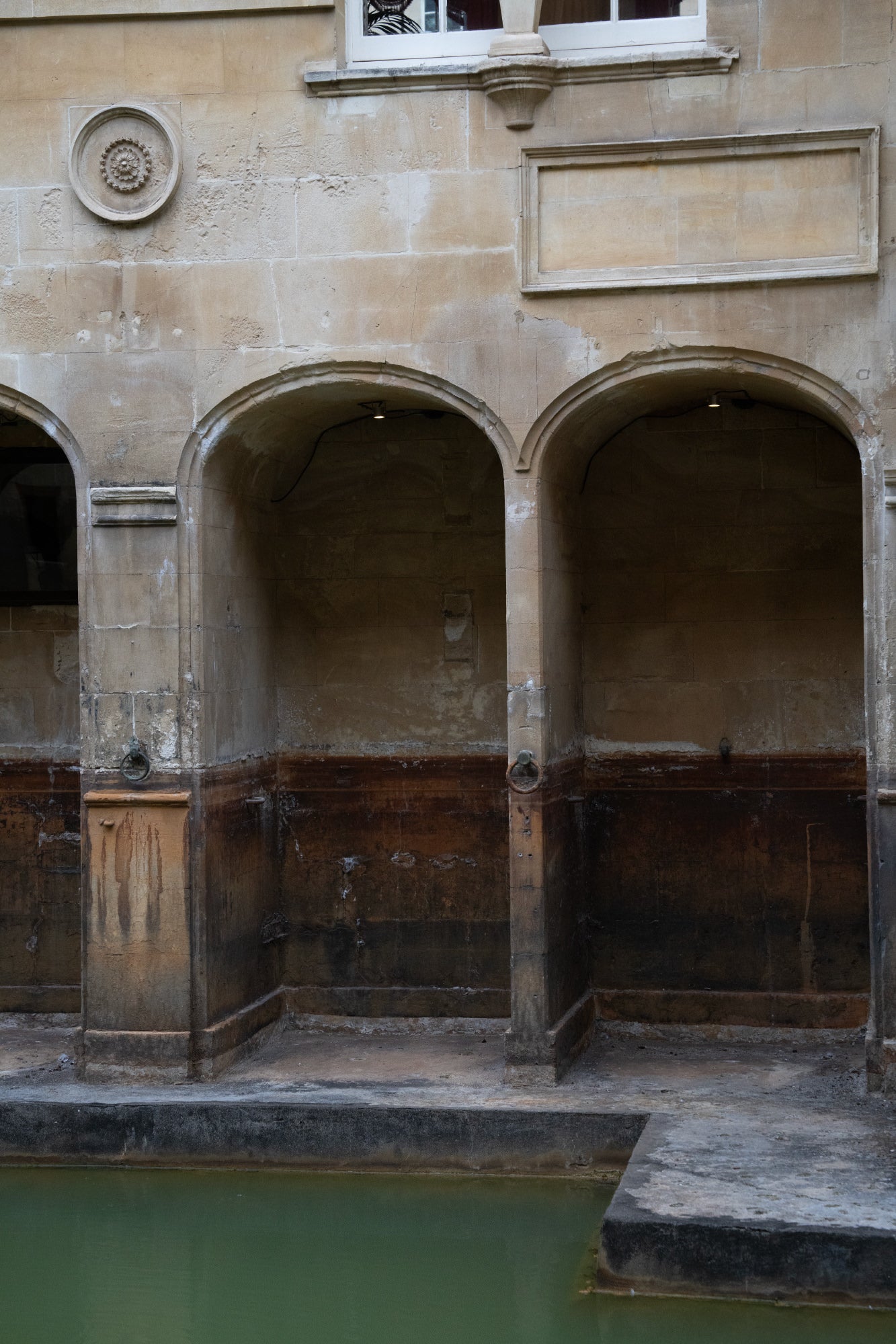Aged stone arches above a green pool, empty alcoves lit faintly.