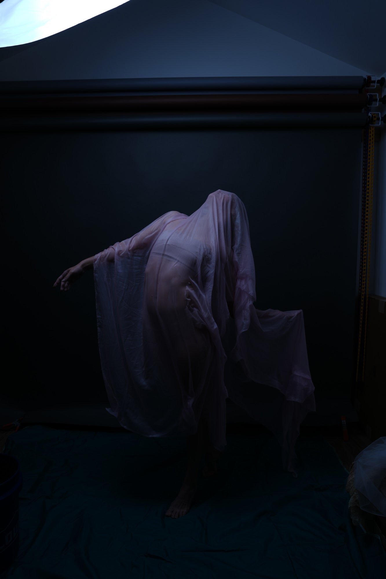 Shrouded figure draped in translucent fabric, posed in a dim studio.