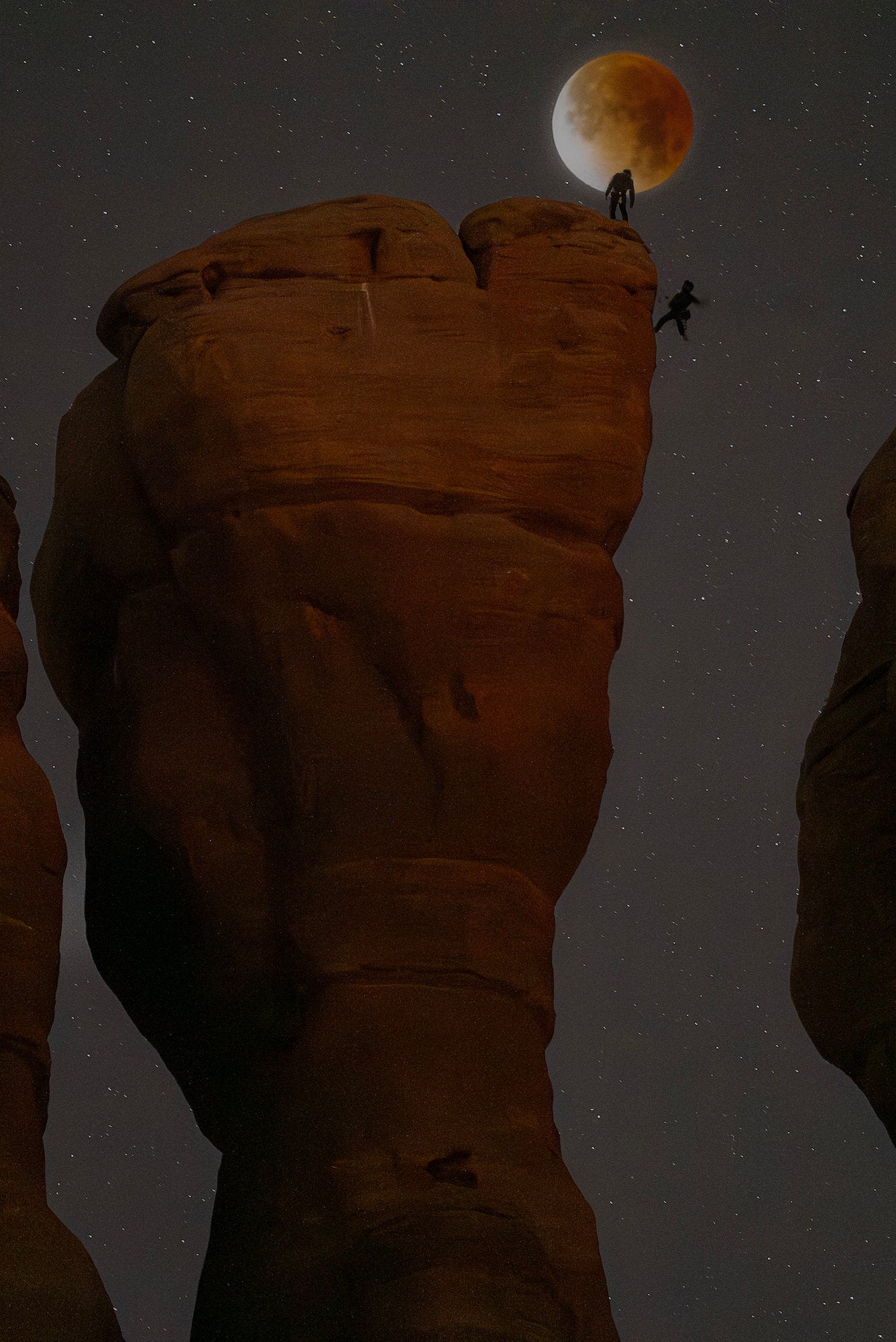 Eclipsed moon above a sandstone pillar as one climber stands and another jumps between towers at night. Eclipsed moon above a sandstone pillar as one climber stands and another jumps between towers at night.