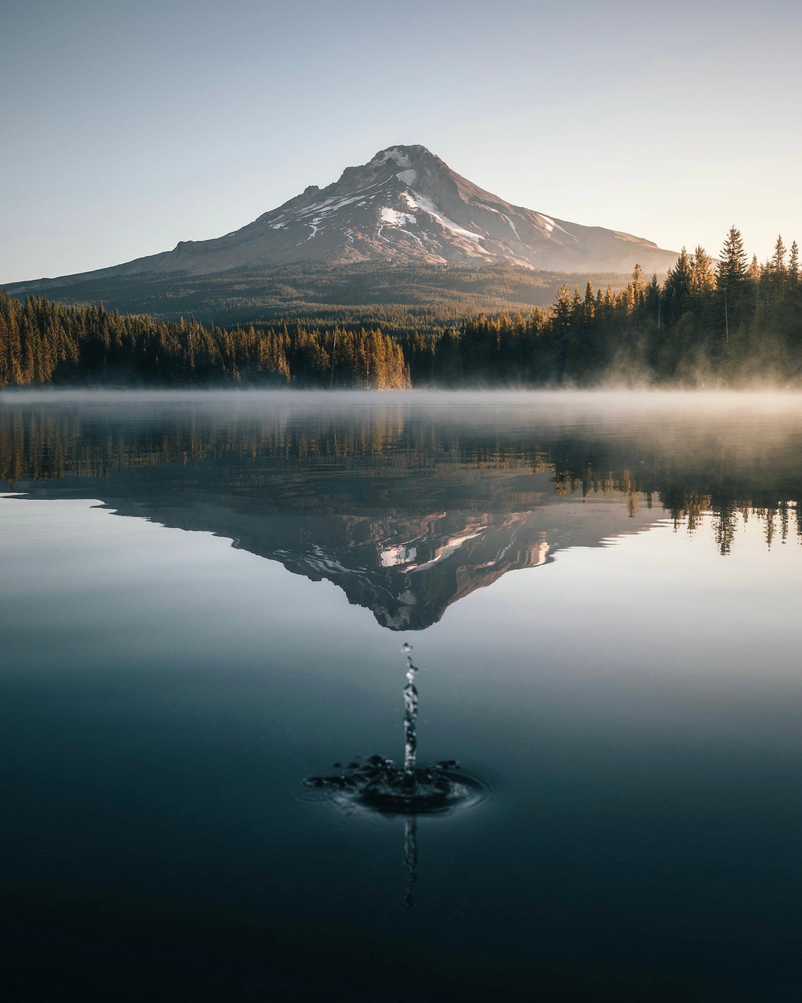 Mount Hood rises above a calm Trillium Lake at sunrise, reflected in the water as a pebble splash creates ripples in the foreground, photographed by Ryan Ditch.