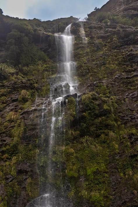 A multi-tiered waterfall threads its way down a mossy volcanic cliff face in a remote New Zealand mountain setting, photographed looking upward by Don Smith.