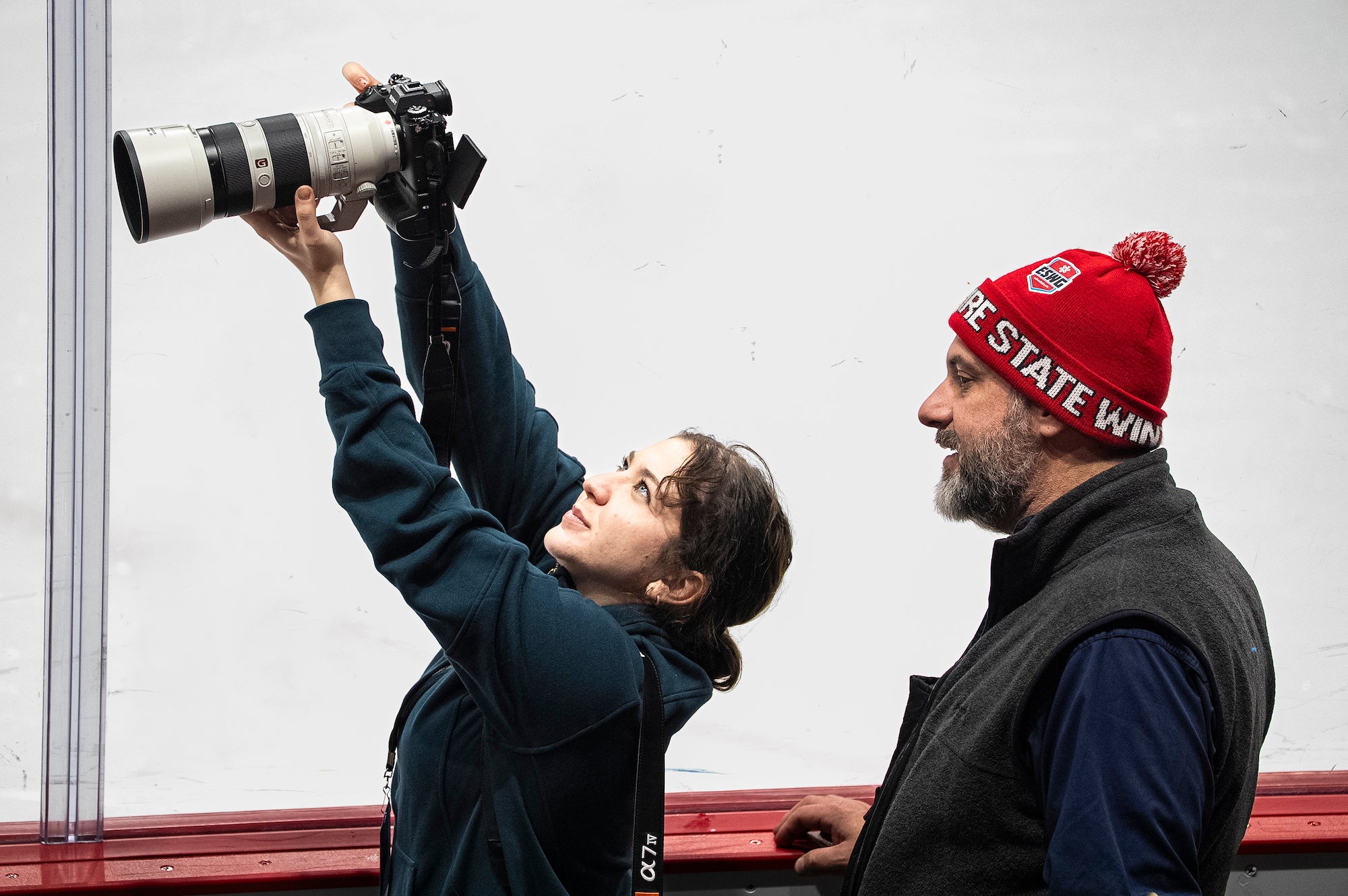 Photographer holds up Sony Alpha camera and G Master lens to photograph ice hockey.