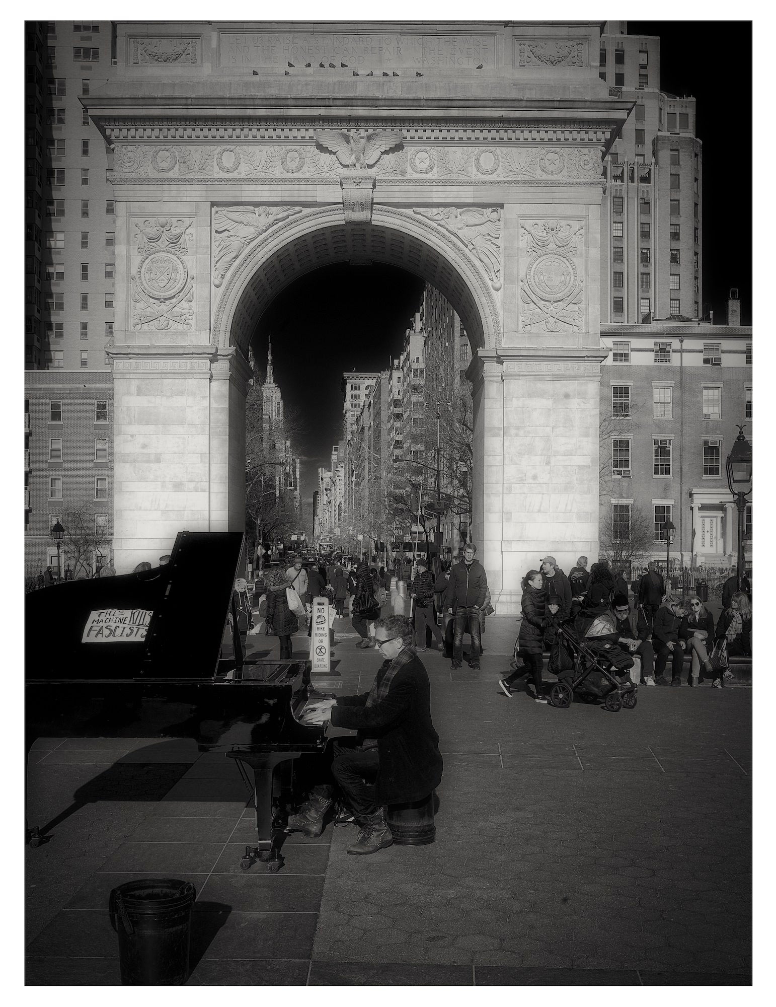 Pianist performing on a grand piano beneath a city arch as crowds pass through the sunlit plaza.