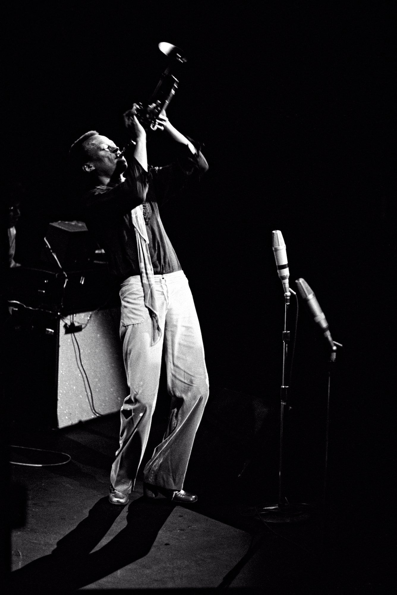 Trumpeter onstage leans back and lifts the horn toward the ceiling; stark lighting against black.