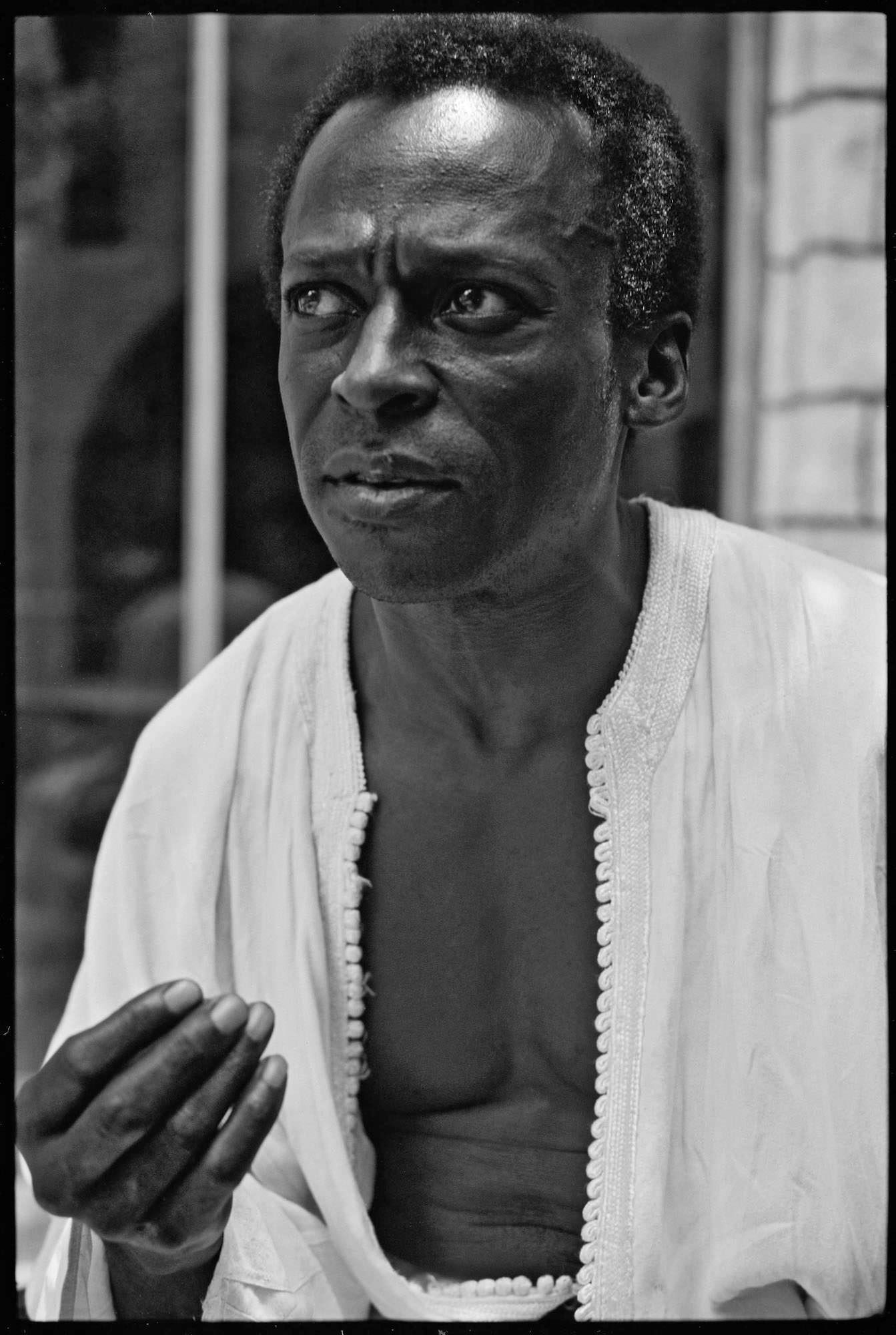 Intimate black‑and‑white portrait of a man in a light robe, mid‑gesture, eyes intense and reflective.