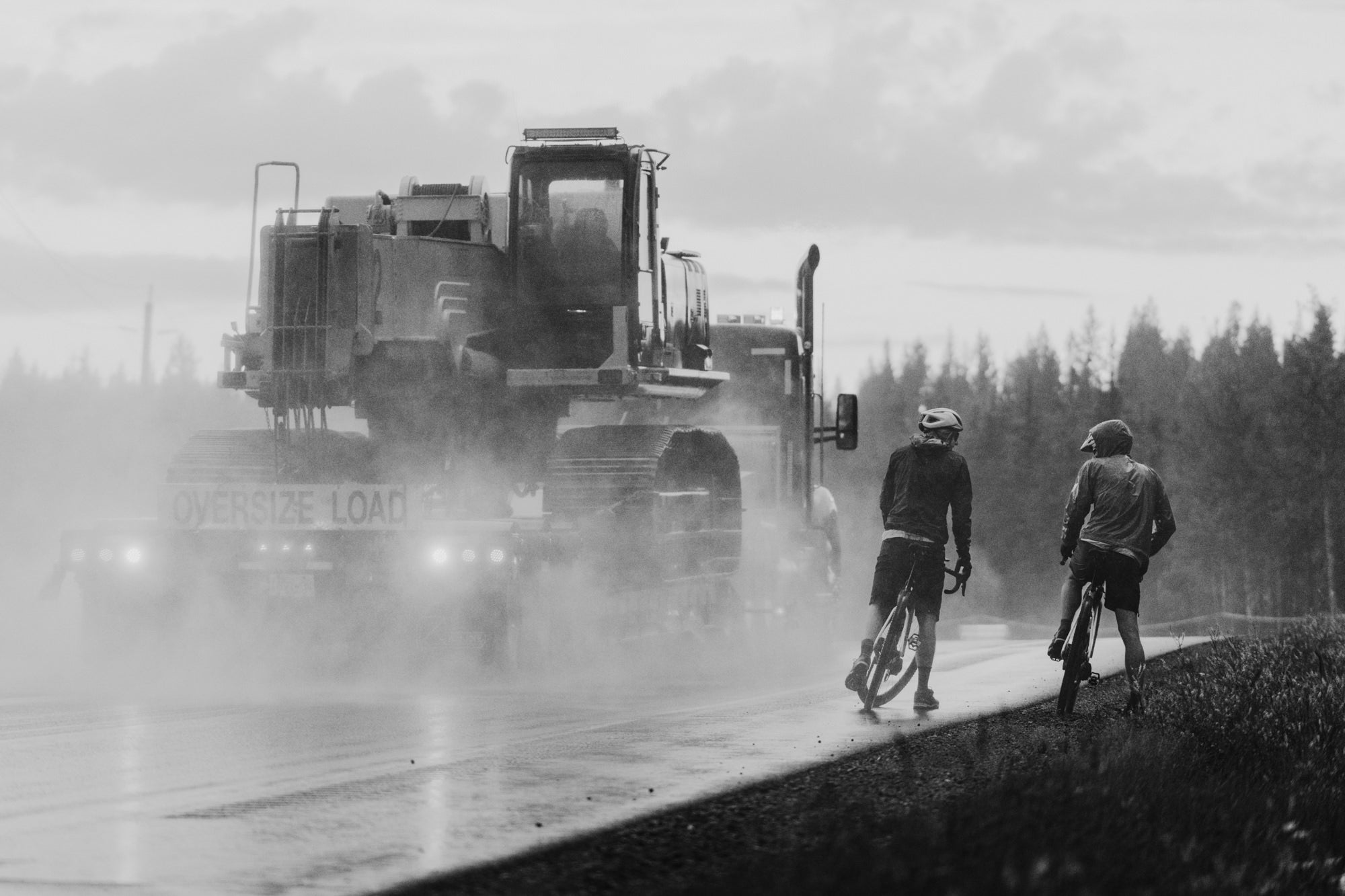 Tommy Caldwell and Alex Honnold biking near a logging truck.