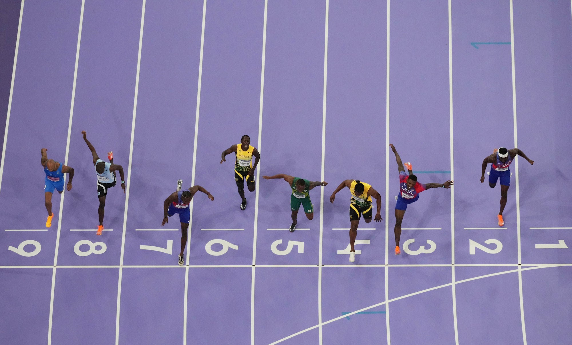 Aerial photo finish of a 100m race, runners crossing a purple track’s line. Aerial photo finish of a 100m race, runners crossing a purple track’s line.