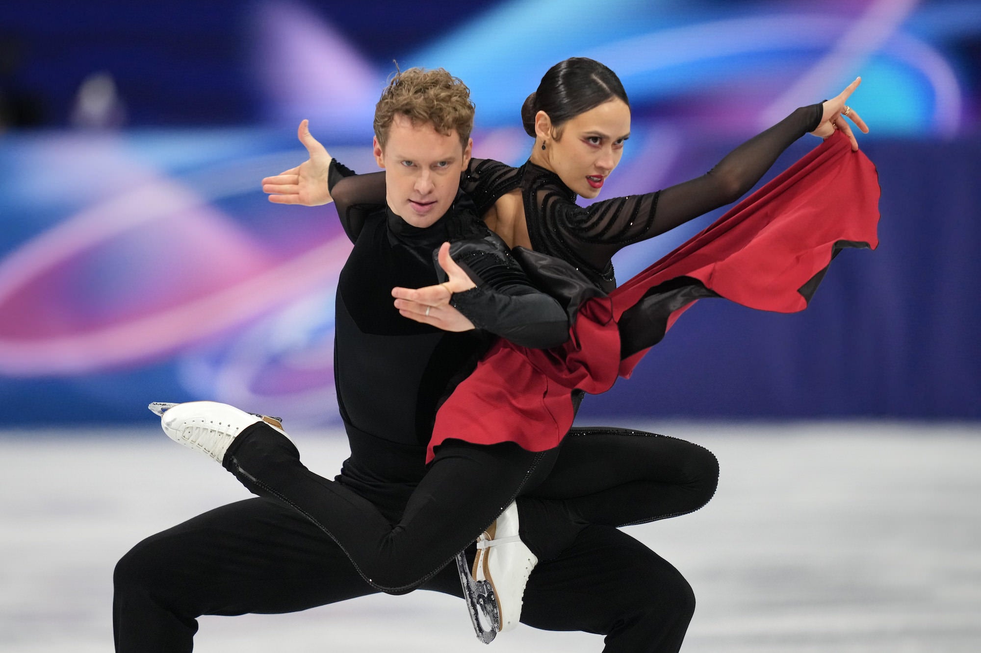 Ice dancers strike a dramatic pose in black outfits with flowing red fabric. Ice dancers strike a dramatic pose in black outfits with flowing red fabric.