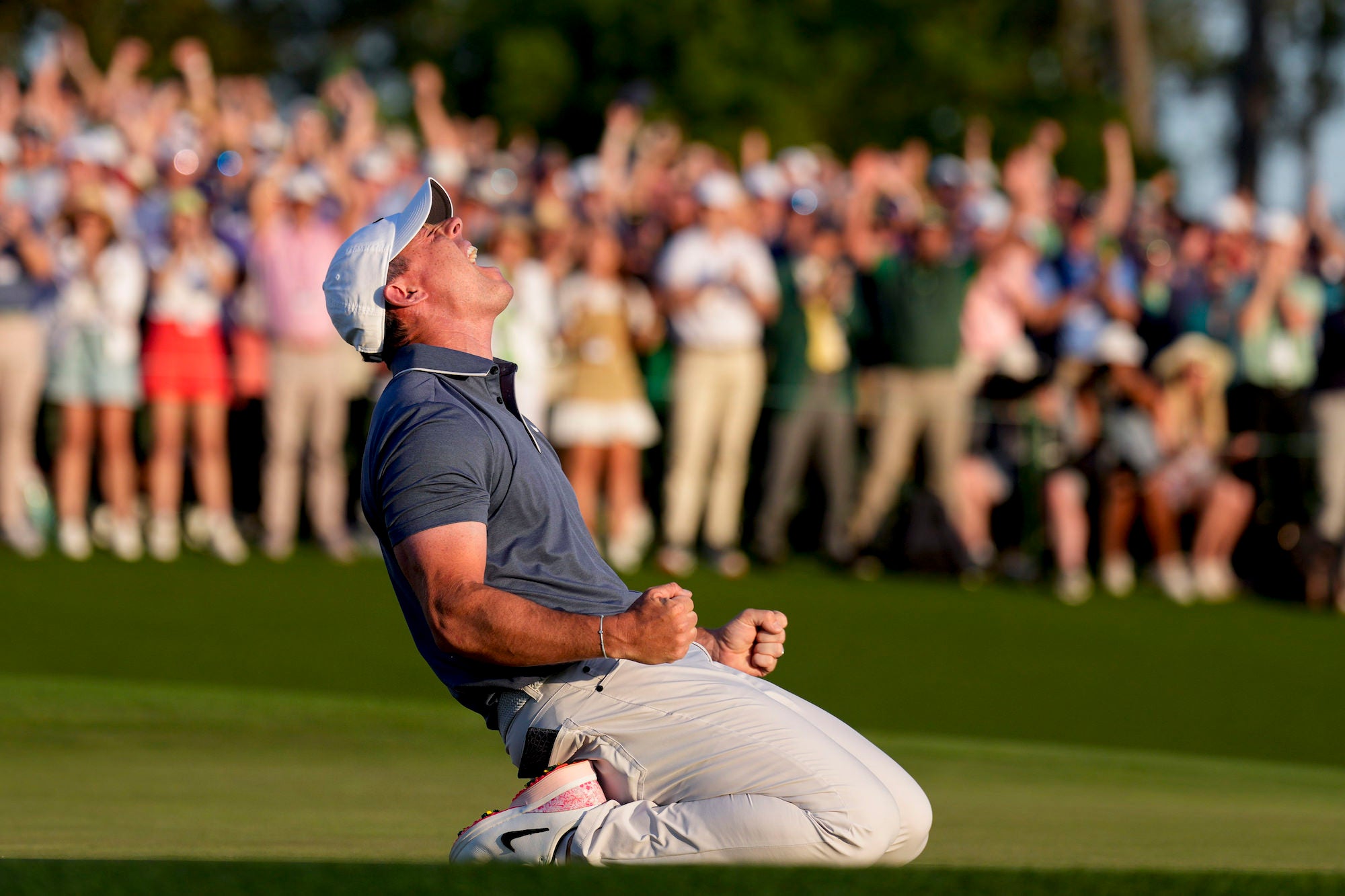 Golfer kneels on the green, fists clenched, roaring as the crowd erupts. Golfer kneels on the green, fists clenched, roaring as the crowd erupts.
