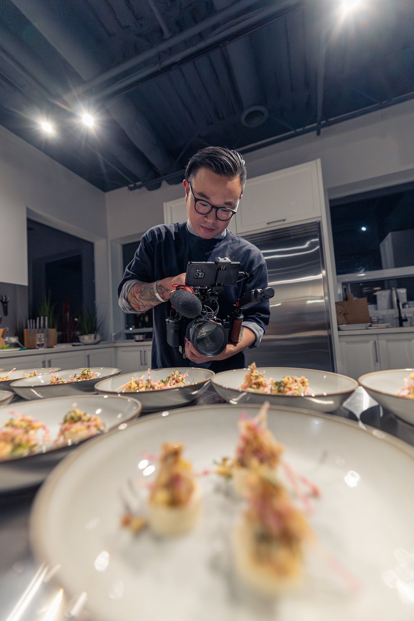 Isaac Tang filming rows of plated appetizers in a commercial kitchen, shallow depth of field.