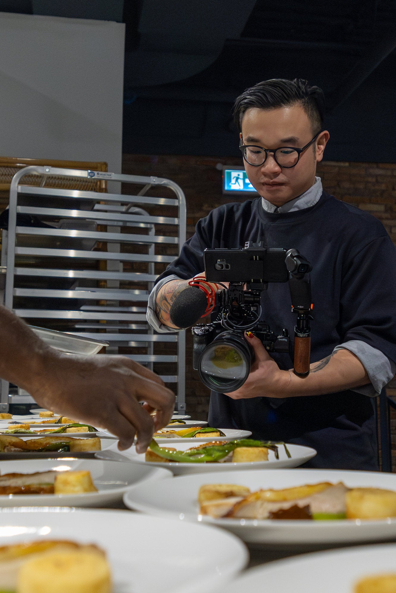 Close-up of Isaac Tang camera rig filming while a chef&rsquo;s hand plates food on white dishes.