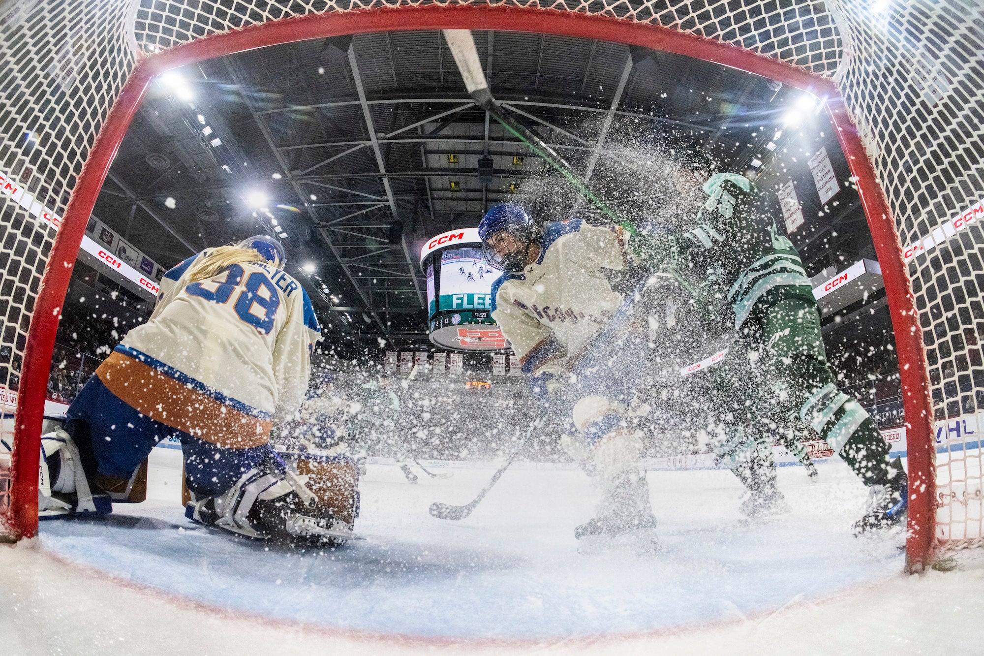 Low angle from inside the net as players crash the crease, ice spray exploding around the goalie.