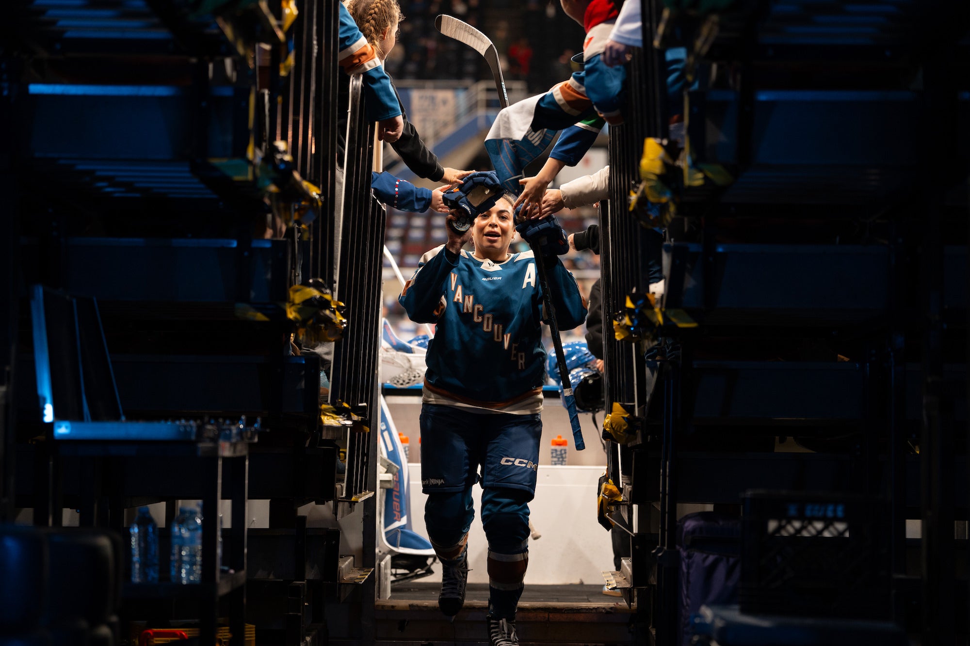 Player in a teal &ldquo;Vancouver&rdquo; jersey high-fives fans while walking up an arena tunnel.