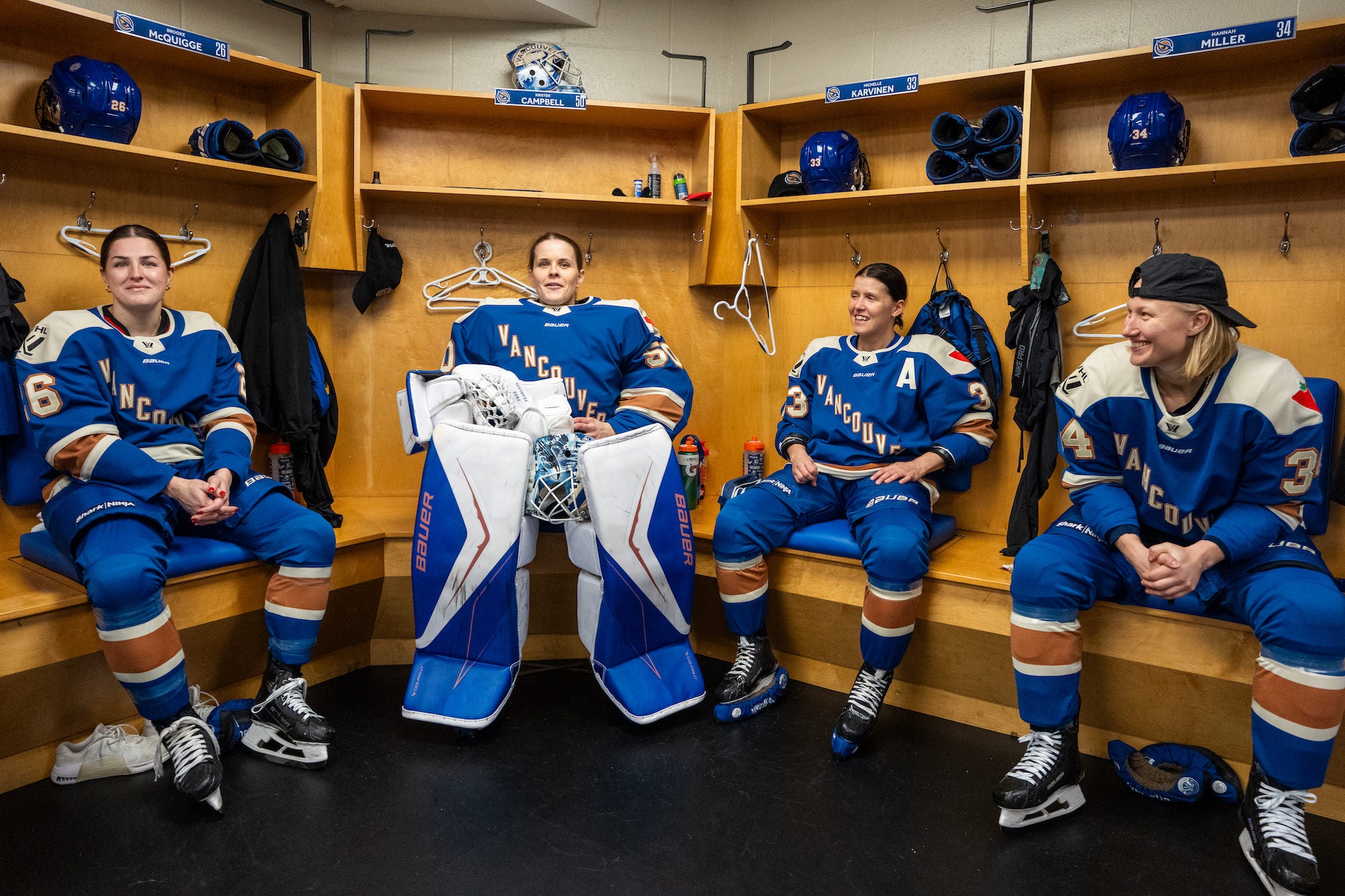 Four players in blue &ldquo;Vancouver&rdquo; uniforms relax and smile in a locker room beside their stalls.