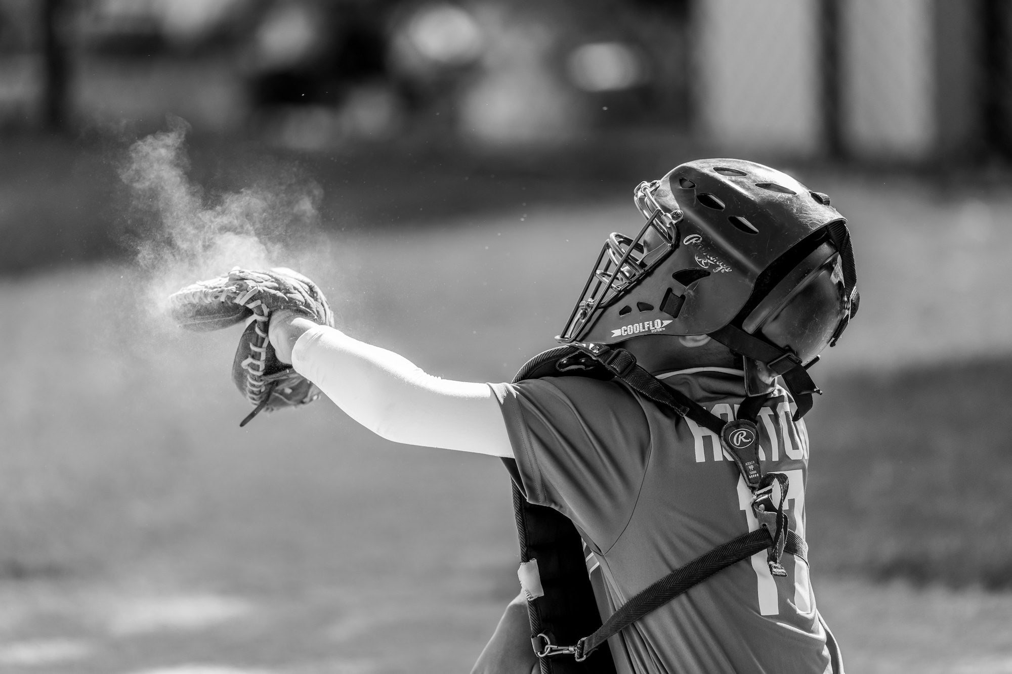 Youth baseball catcher extends a gloved hand as chalk dust puffs, black-and-white action.
