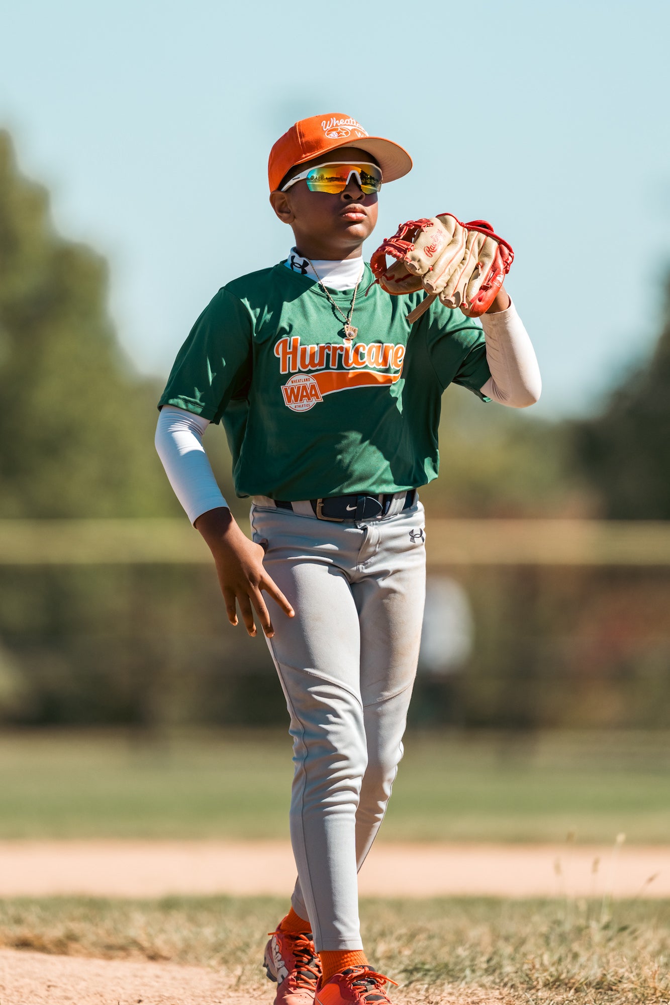 Infielder in green jersey waits between plays, glove raised, soft background bokeh.