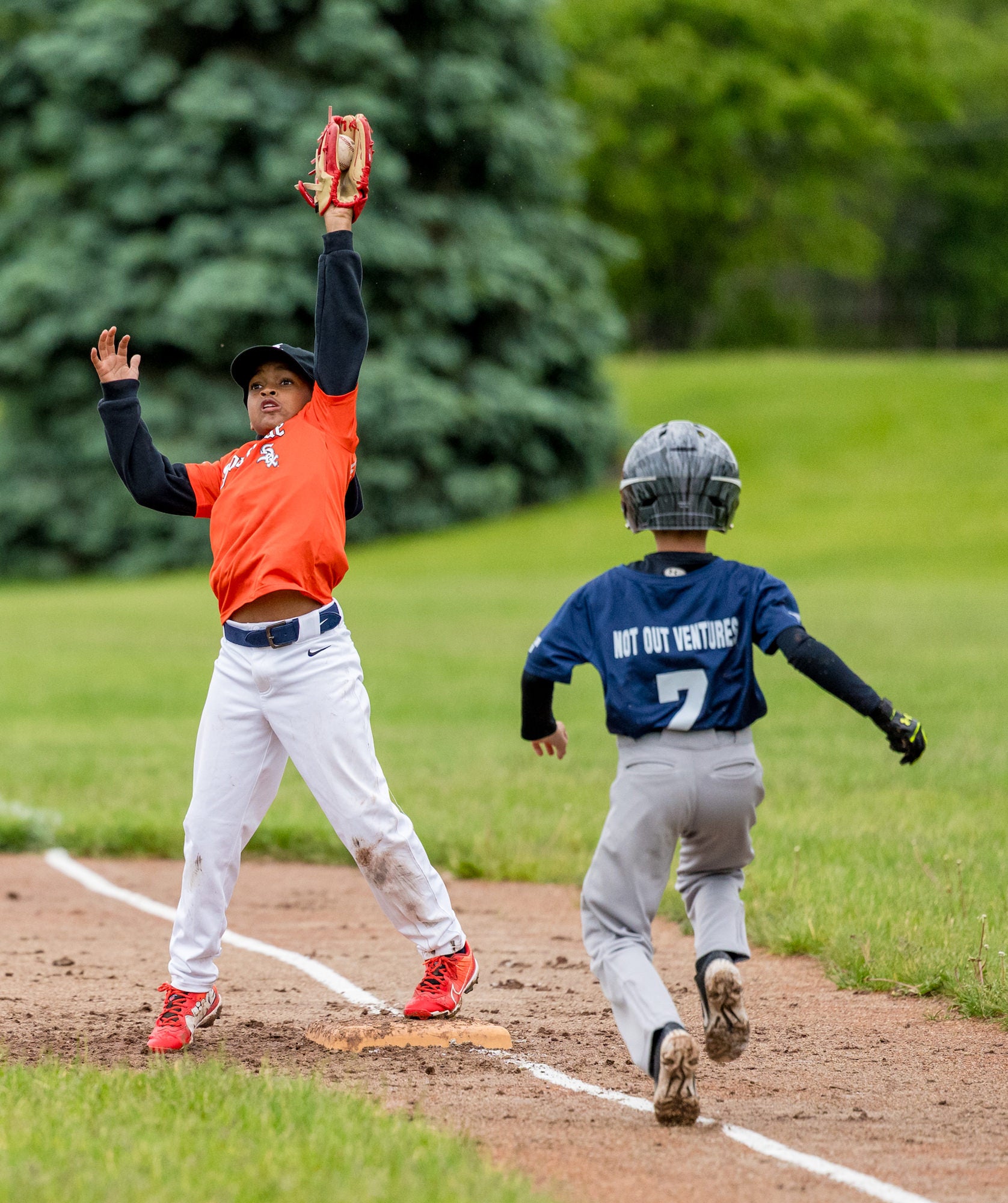 First baseman leaps to snag a high throw as a runner sprints to first on a damp infield.