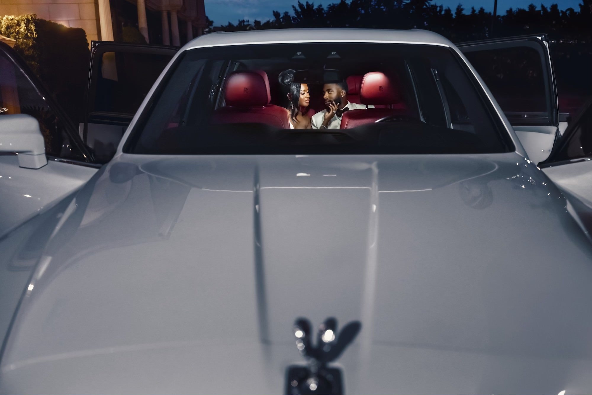View from the hood of a white car looking into the back seat where a couple is sitting View from the hood of a white car looking into the back seat where a couple is sitting