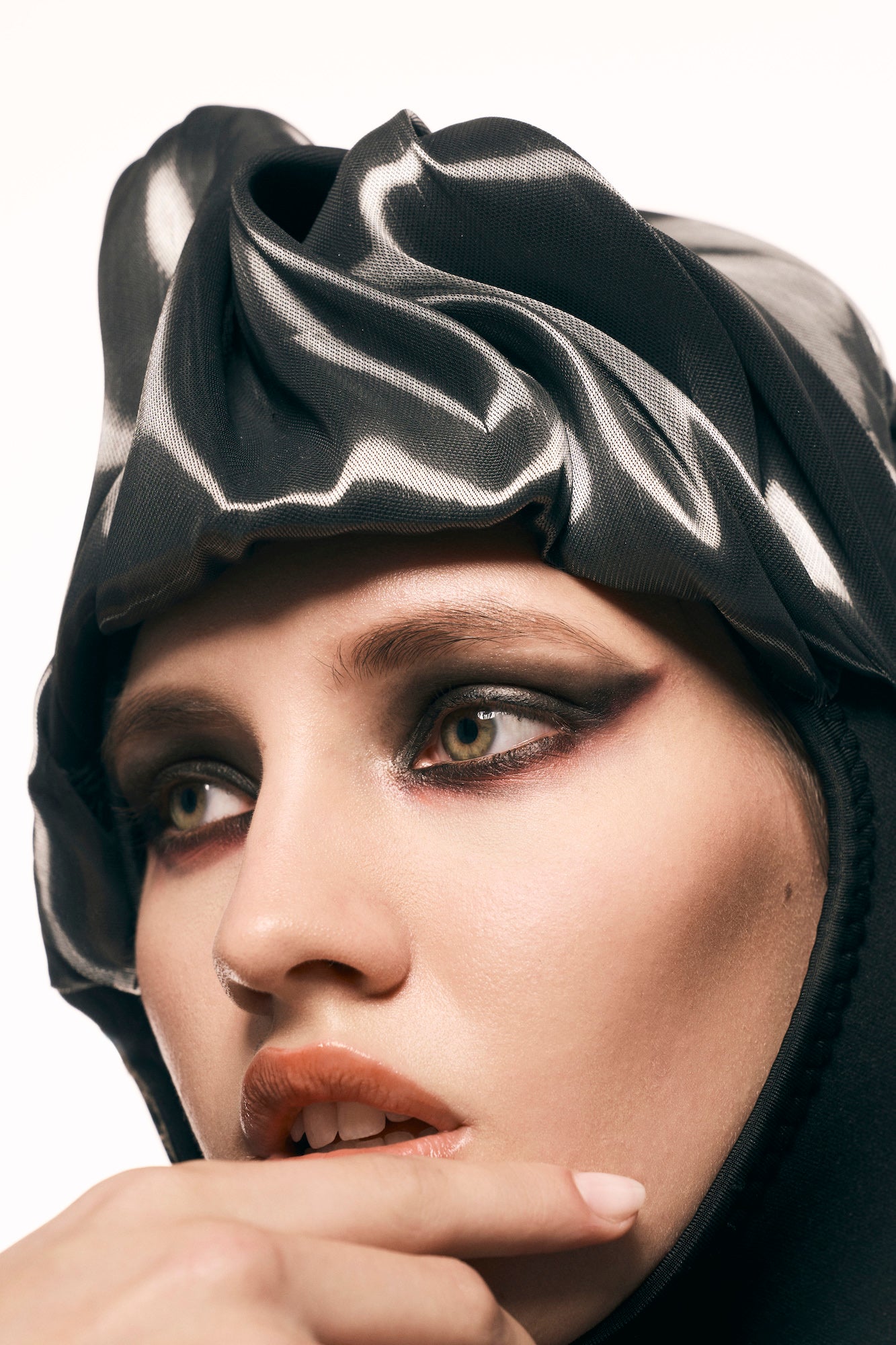 Beauty close-up of a model in dark smoky eye makeup and a sculpted black headwrap, finger at her lips. Beauty close-up of a model in dark smoky eye makeup and a sculpted black headwrap, finger at her lips.