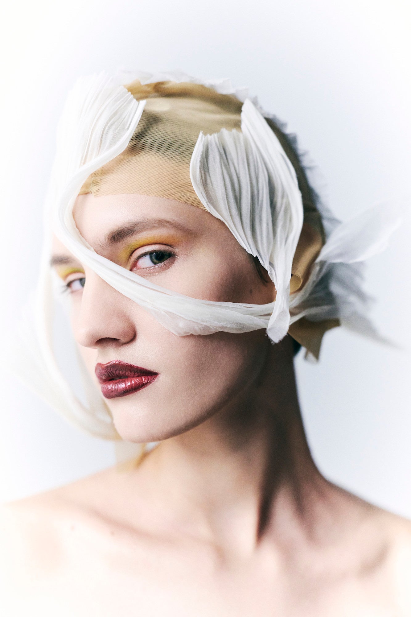 Beauty portrait of a model with yellow eyeshadow and deep red lips, head wrapped in sheer white fabric. Beauty portrait of a model with yellow eyeshadow and deep red lips, head wrapped in sheer white fabric.