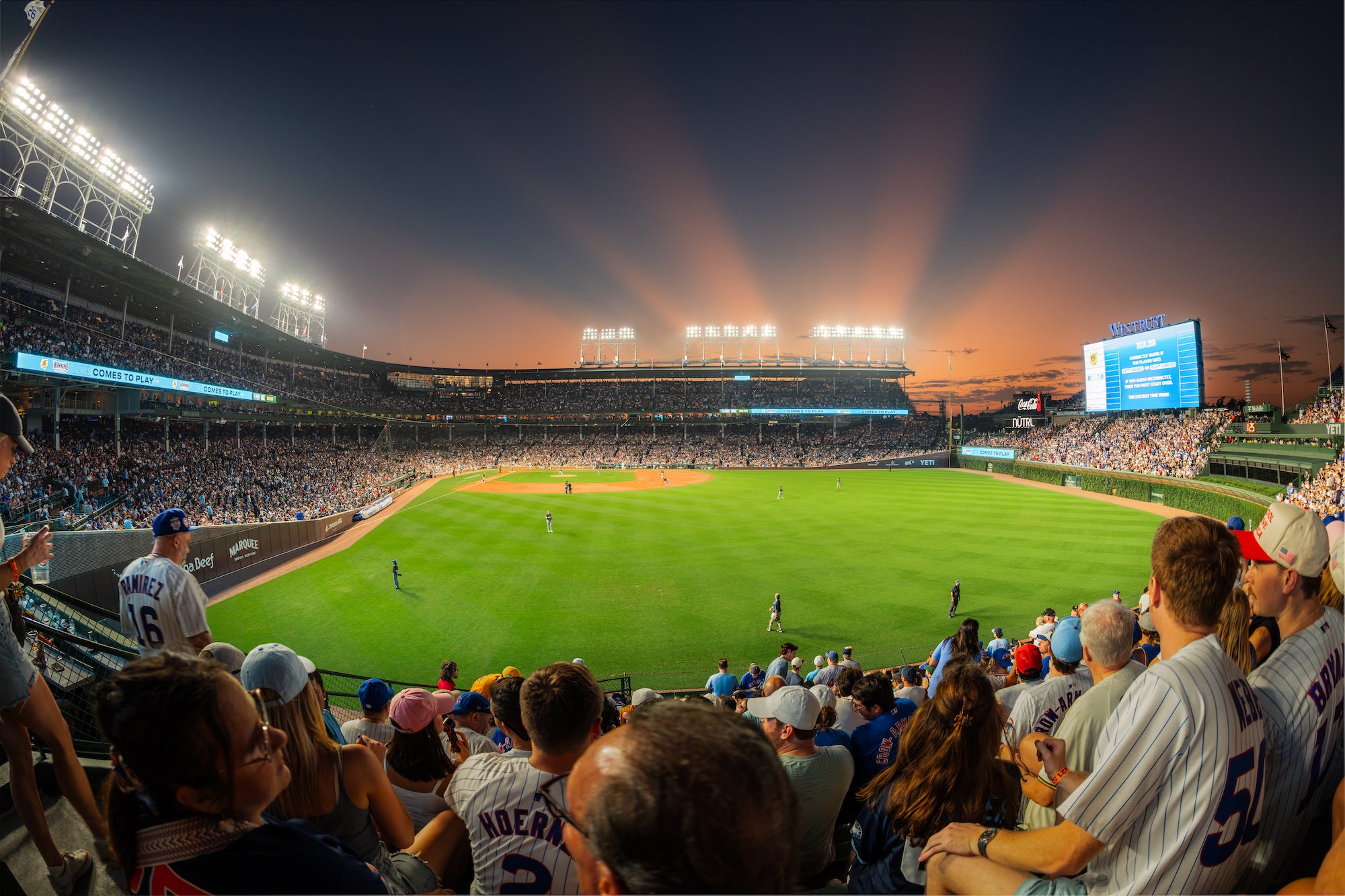 A packed baseball stadium glows beneath bright lights at sunset, photographed by Mike Meyers.