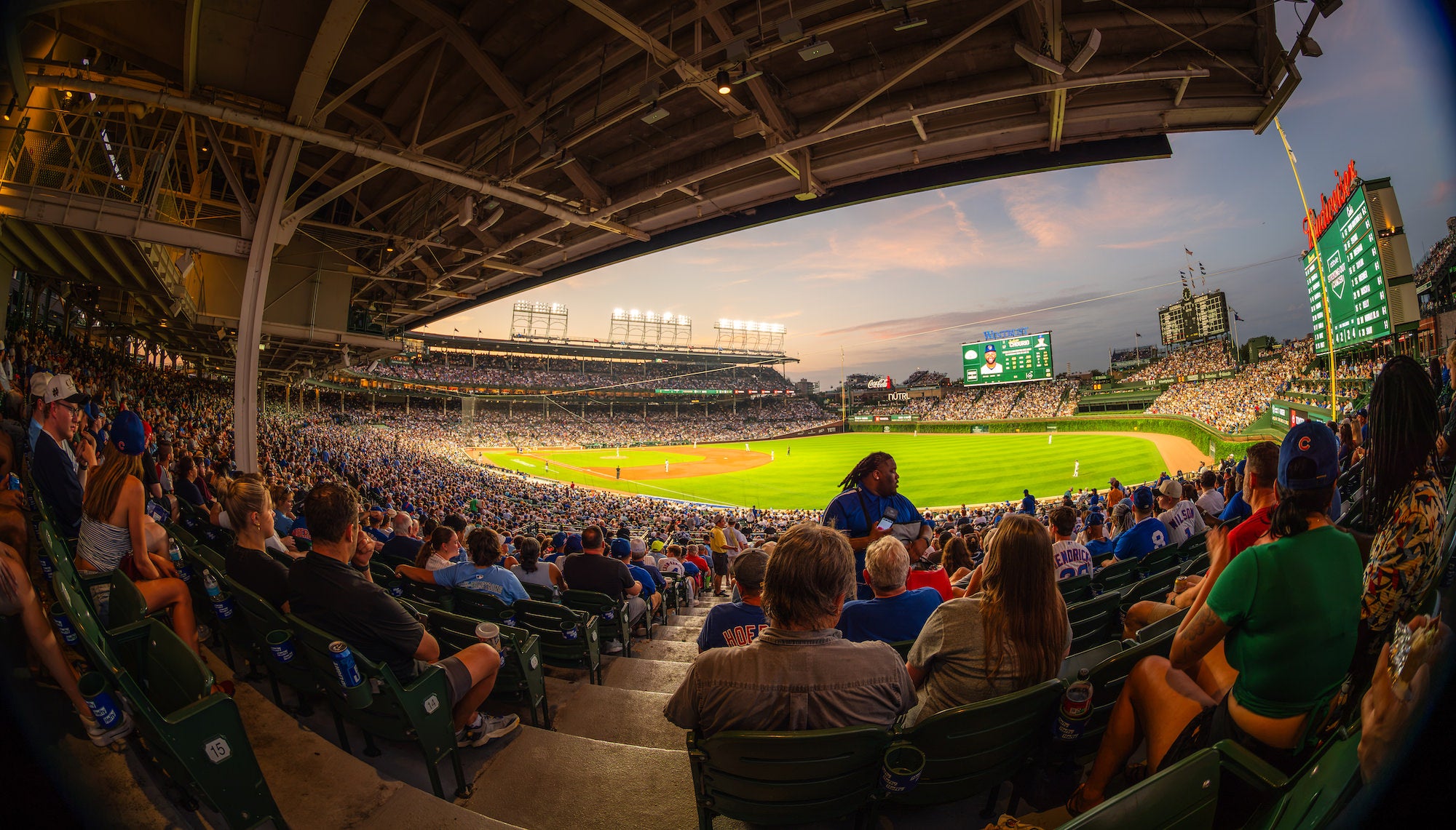 Fans fill covered stadium seats as a baseball game unfolds on the brightly lit field beneath a pink-and-blue evening sky. Photo by Mike Meyers. Alpha 7R V. 8-14mm f/3.5 Fisheye G. 1/40-sec. f/3.5. ISO 100.
