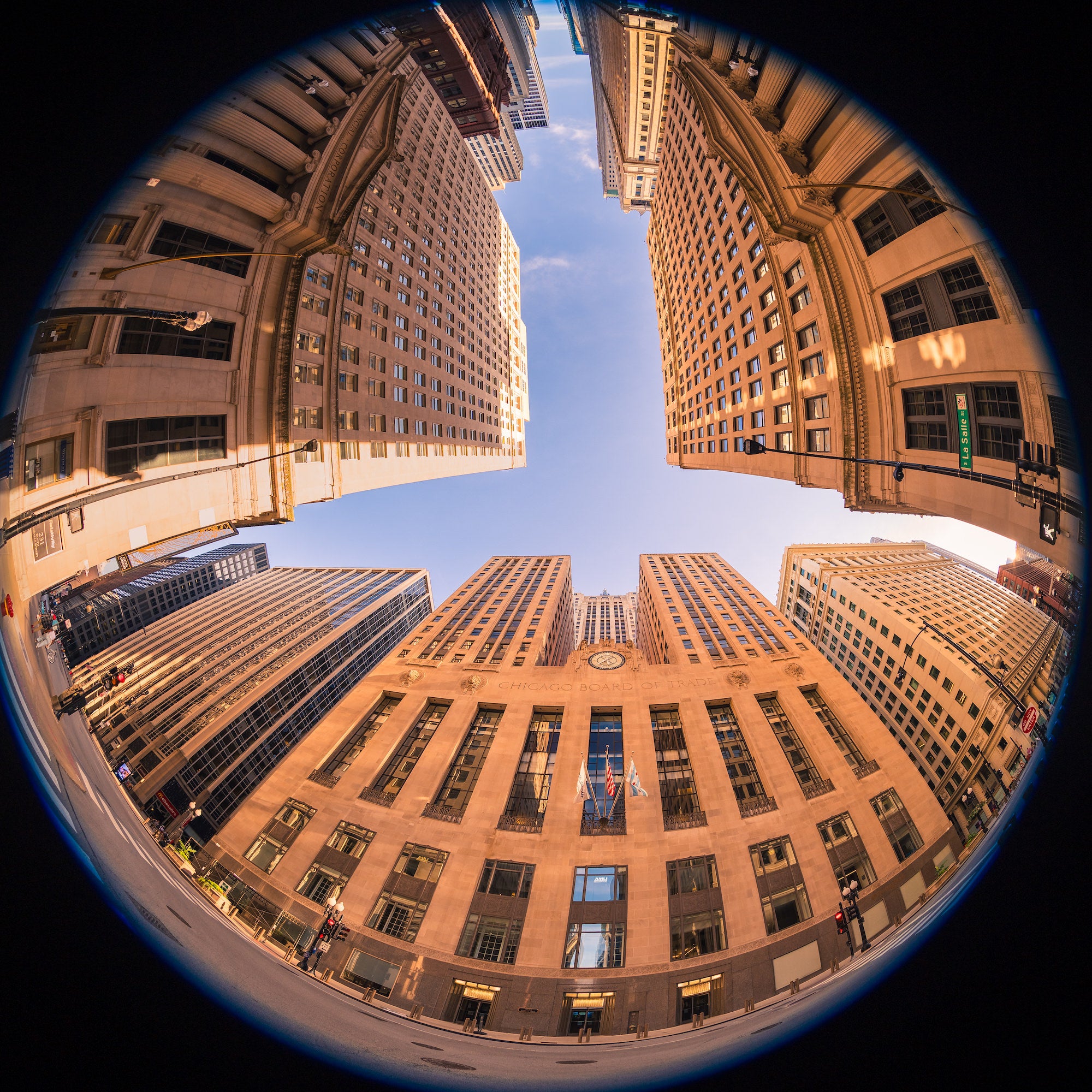 Fisheye view looking upward between tall office buildings, their warm stone fa&ccedil;ades curving around a bright blue sky. Photo by Mike Meyers. Alpha 1. 8&ndash;14mm f/3.5 Fisheye G. 1/250-sec. f/3.5. ISO 100.