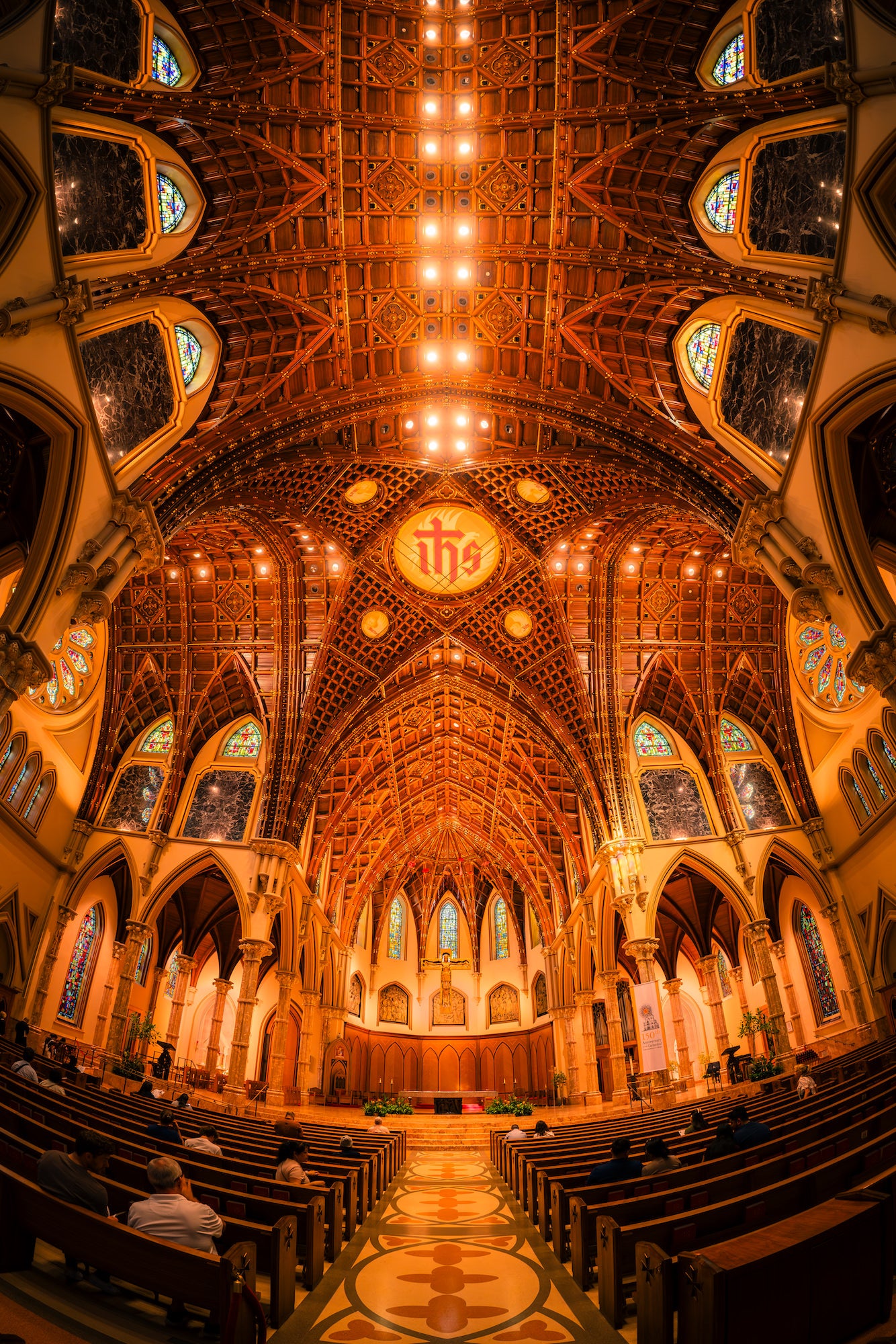 Warmly lit church interior with a soaring wood ceiling, stained-glass windows, stone arches, and rows of pews leading to the altar. Photo by Mike Meyers. Alpha 1. 8-14mm f/3.5 Fisheye G. 1/320-sec. f/3.5. ISO 1000.