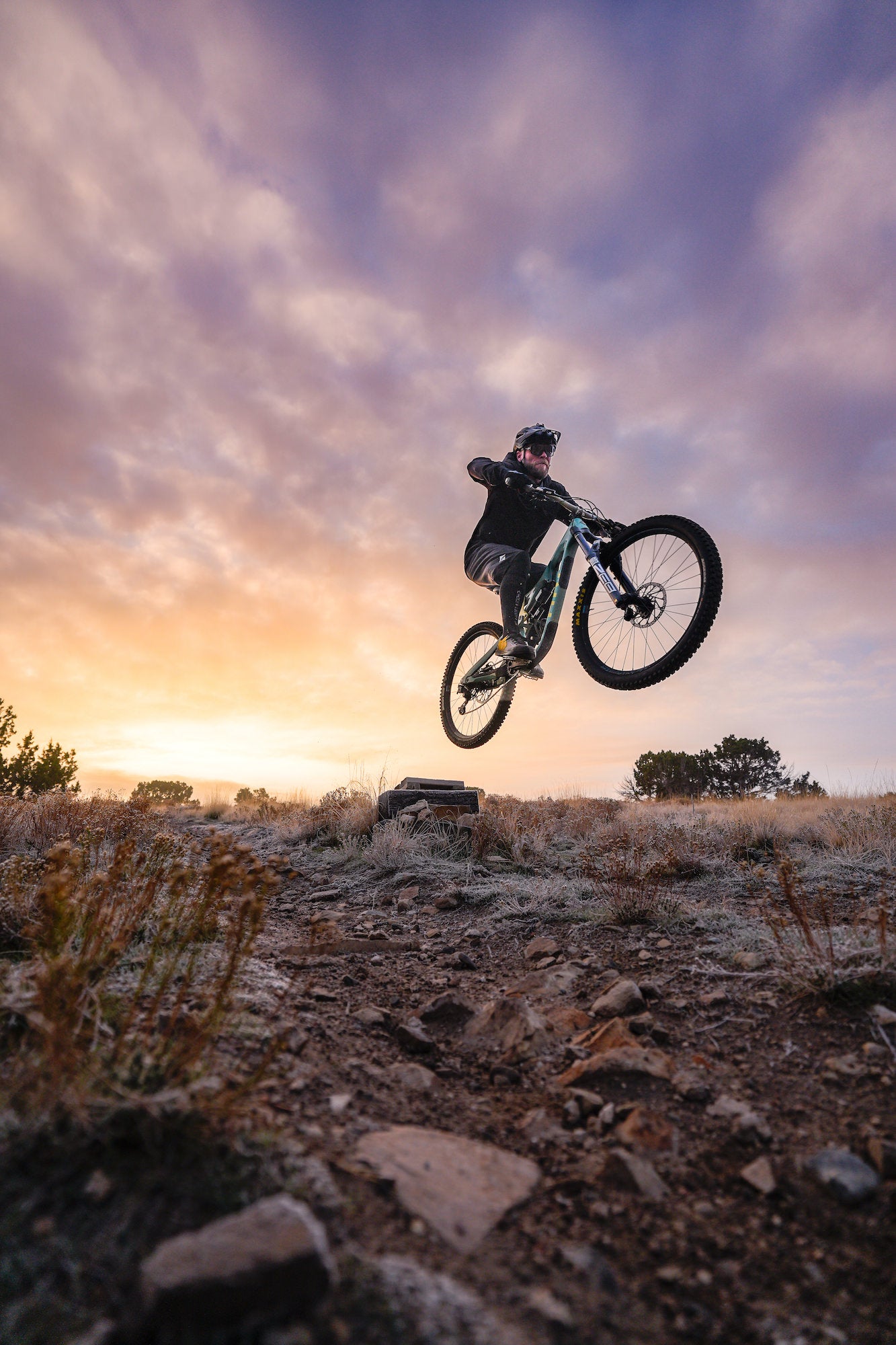Mountain biker jumping over rocky terrain in front of a colorful sky.