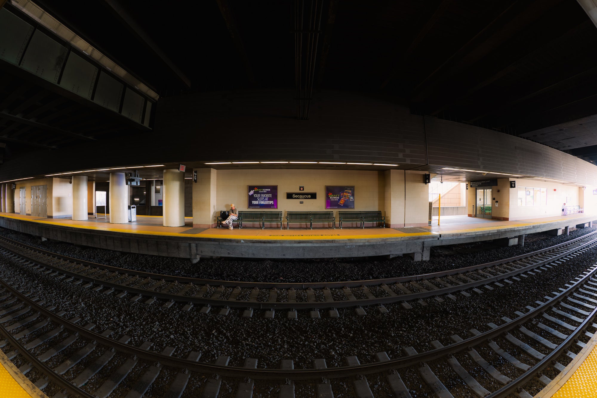Wide fisheye view of a Secaucus train station platform and curving railroad tracks, photographed by Nick Di Giugno.