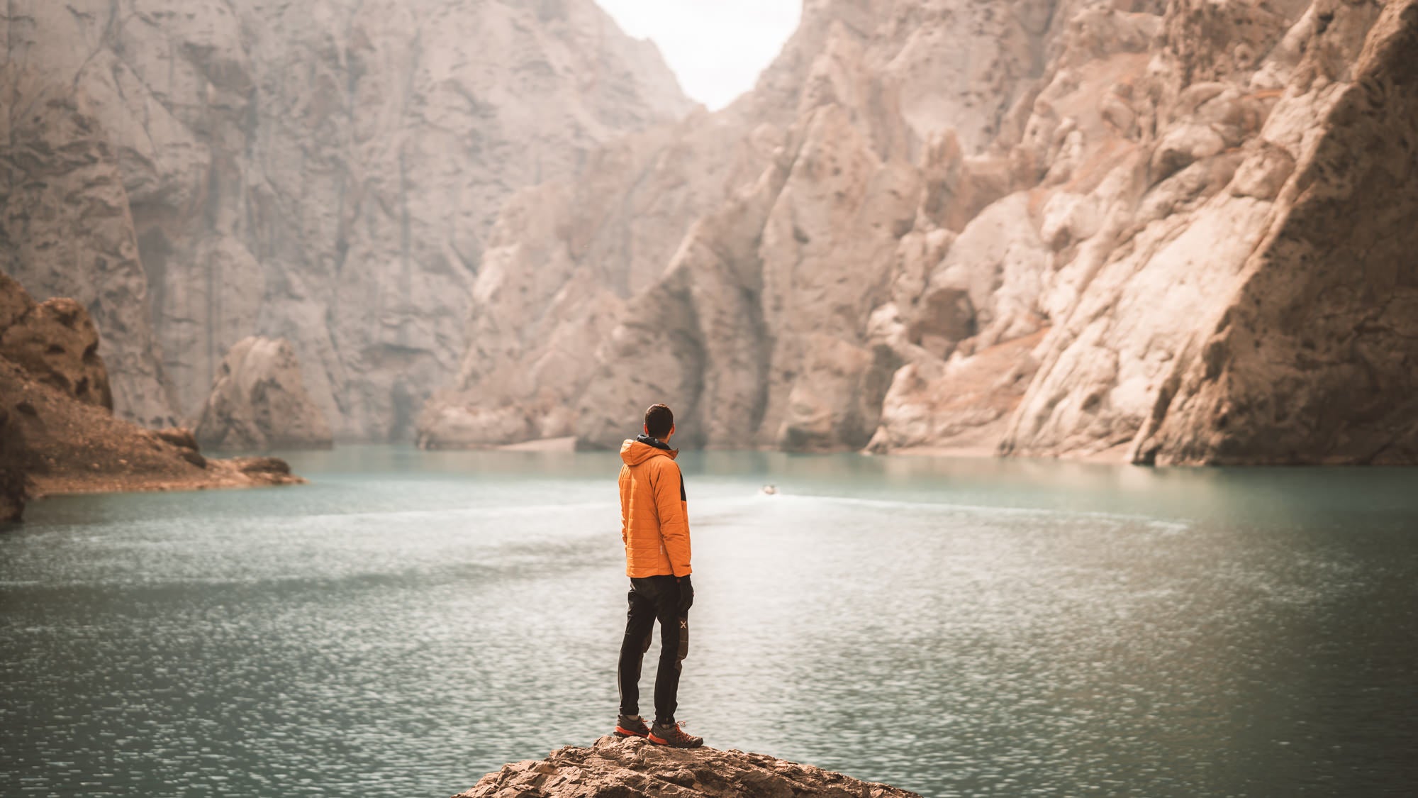 Man standing on rock in yellow jacket with beautiful lake and mountain landscape in the background