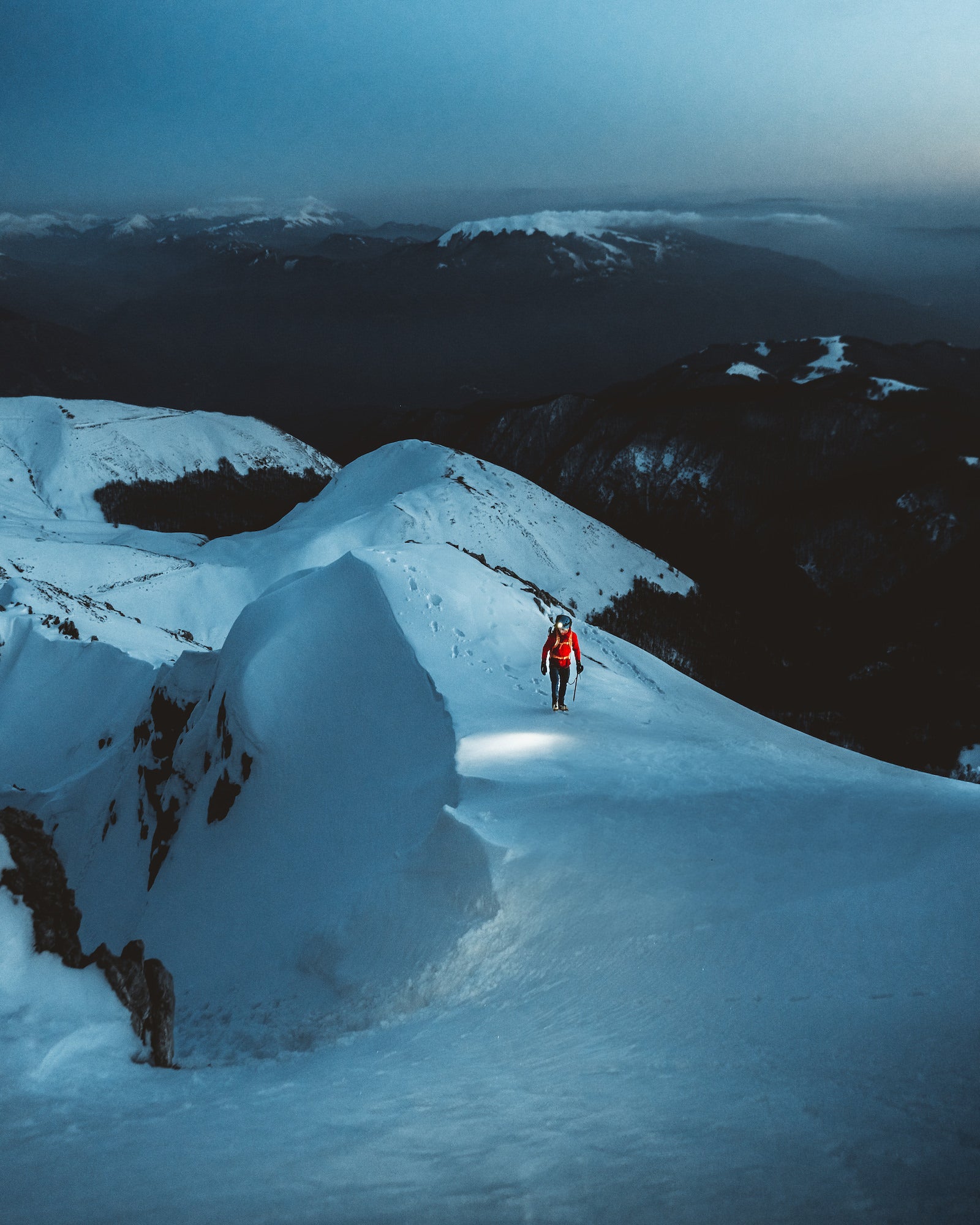 Blue hour image of a person walking along a snowy mountainscape